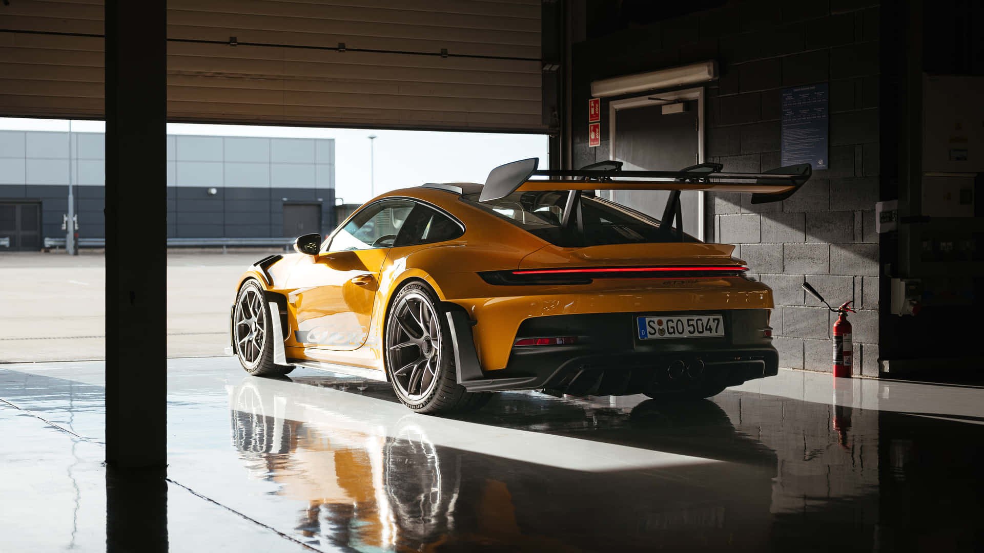  壁紙 — 一輛充滿活力的橙色保時捷911 GT3 RS在自然光下閃閃發光，停放在一個帶有濕滑反光地板的時尚車庫中。
