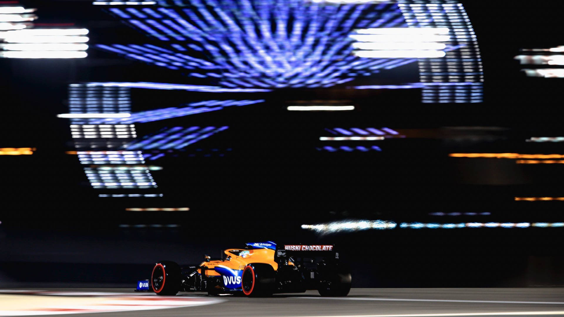 一級方程式賽車在夜間奔馳，賽道上留下光跡 — F1 壁紙