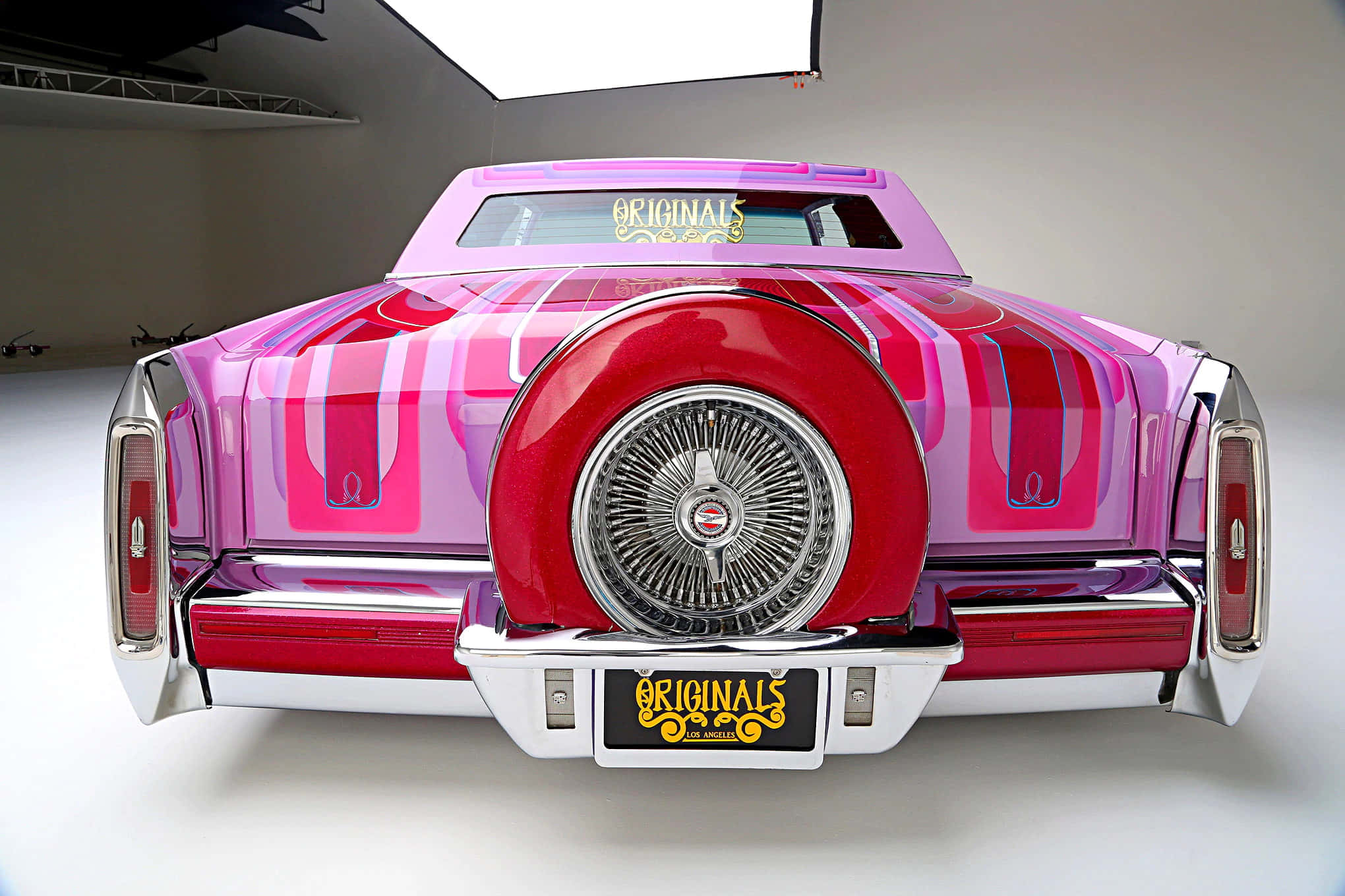 Cadillac Fleetwood 桌布 壁紙 — 一輛充滿活力的粉紅色和紅色定制經典汽車，帶有鍍鉻細節和 'Originals' 品牌，在工作室從後方拍攝。