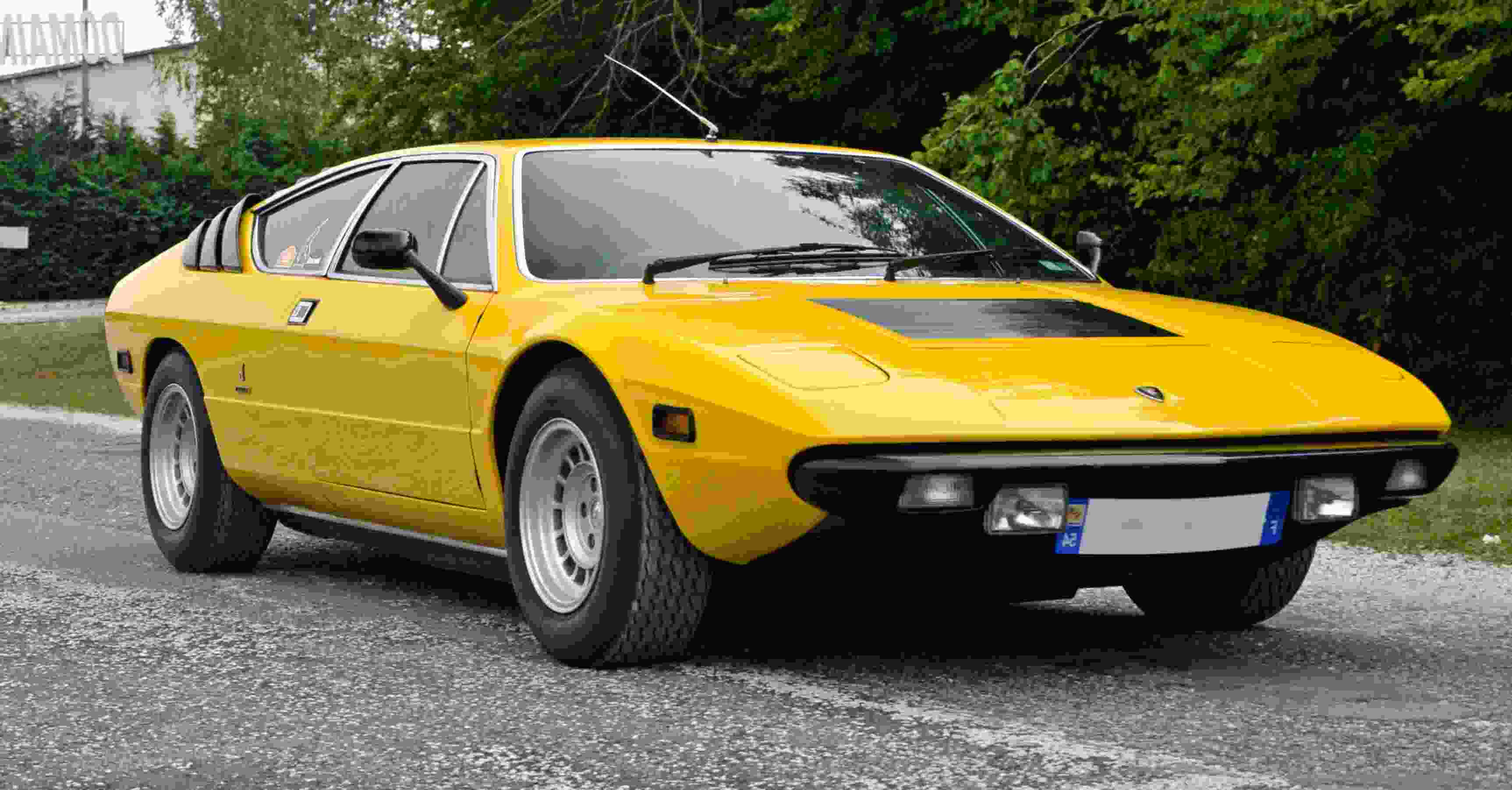 Lamborghini Urraco 桌布 壁紙 — 一輛充滿活力的黃色經典跑車停放在碎石車道上，周圍環繞著茂密的綠樹。