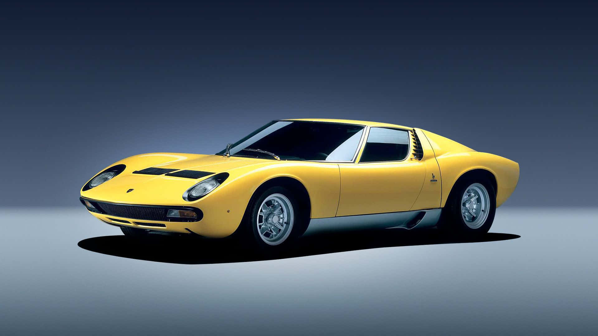 Lamborghini Miura 桌布 壁紙 — 一輛充滿活力的黃色藍寶堅尼Miura跑車，帶有黑色賽車條紋，在漸變灰色工作室背景前蓄勢待發。