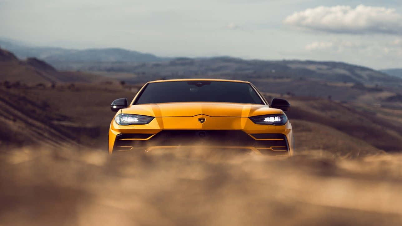 Lamborghini Urus 桌布 壁紙 — 一輛充滿活力的黃色藍寶堅尼在塵土飛揚的田野中疾馳，背景是起伏的丘陵和多雲的天空。