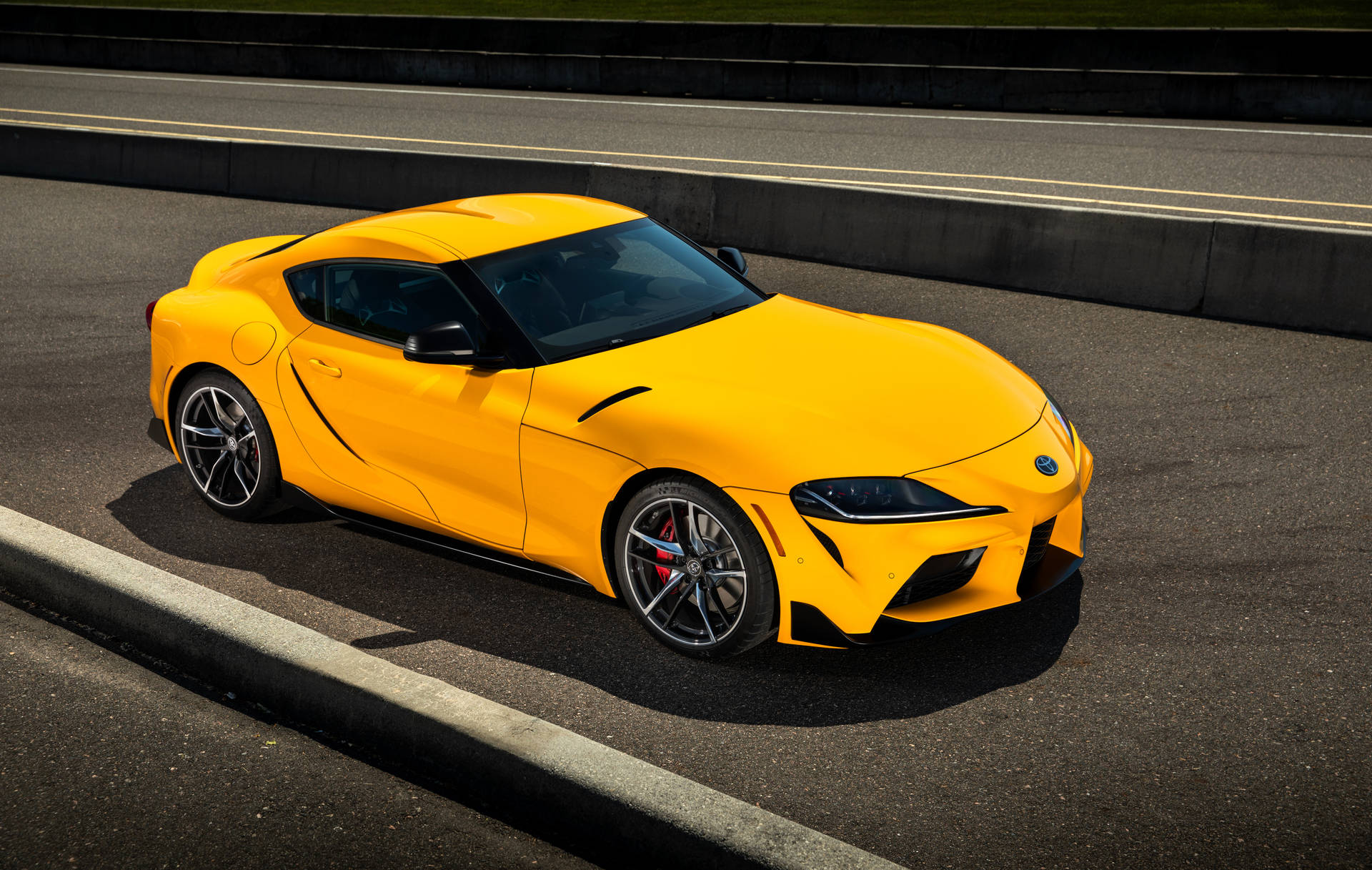黃色跑車在瀝青賽道上於陽光下奔馳。 — Toyota Supra 壁紙