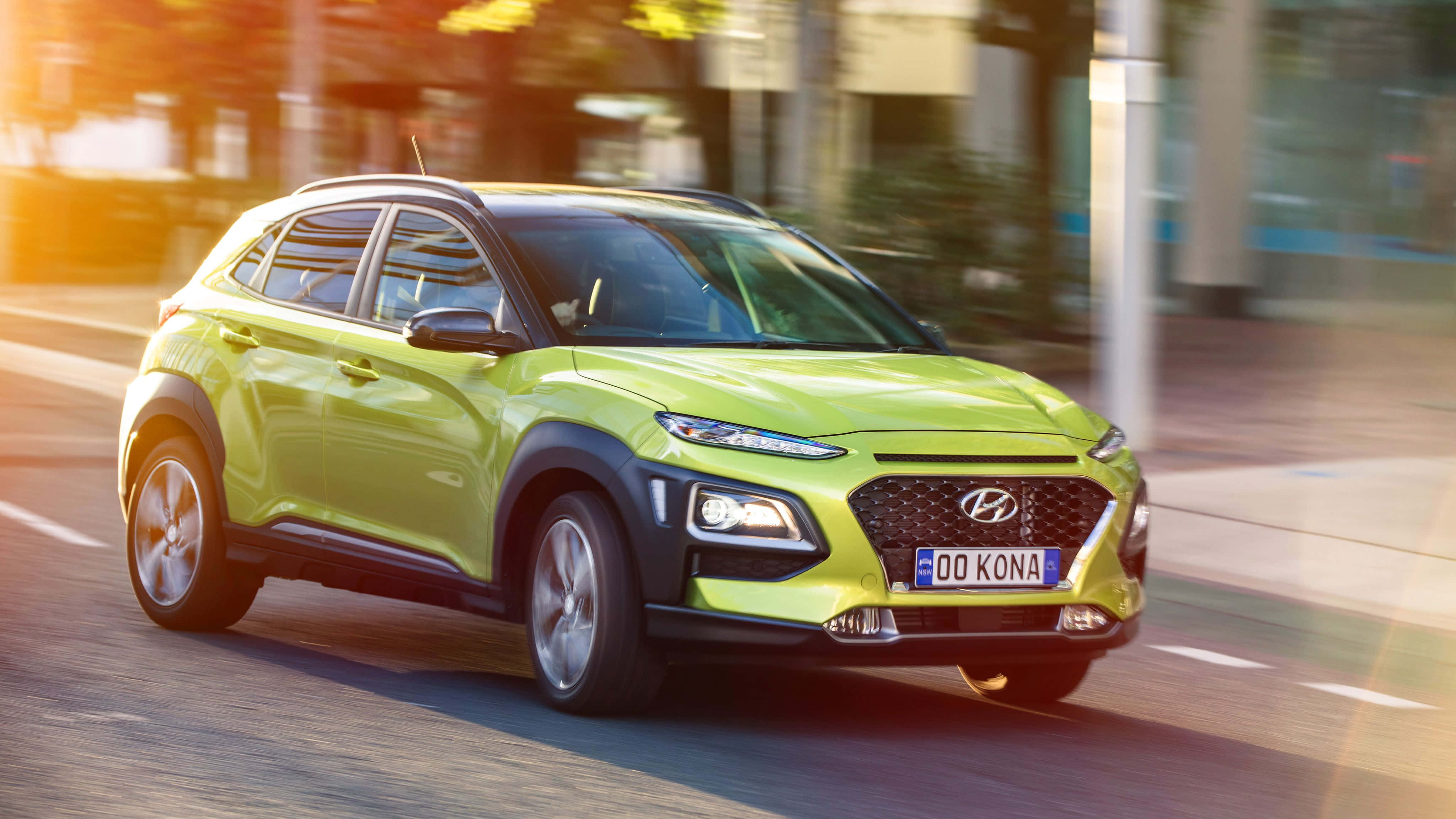 Hyundai Kona 桌布 壁紙 — 一輛充滿活力的萊姆綠色現代Kona SUV在陽光明媚的城市街道上疾馳，背景呈現動態模糊效果。