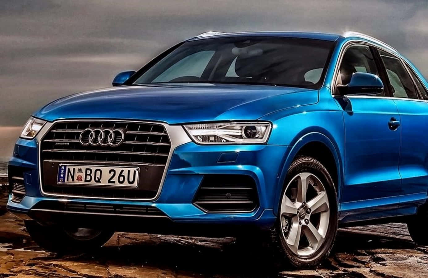 Audi Q5 桌布 壁紙 — 一輛充滿活力的藍色奧迪Q3 SUV在陰沉多雲的天空下，停在崎嶇潮濕的地形上。