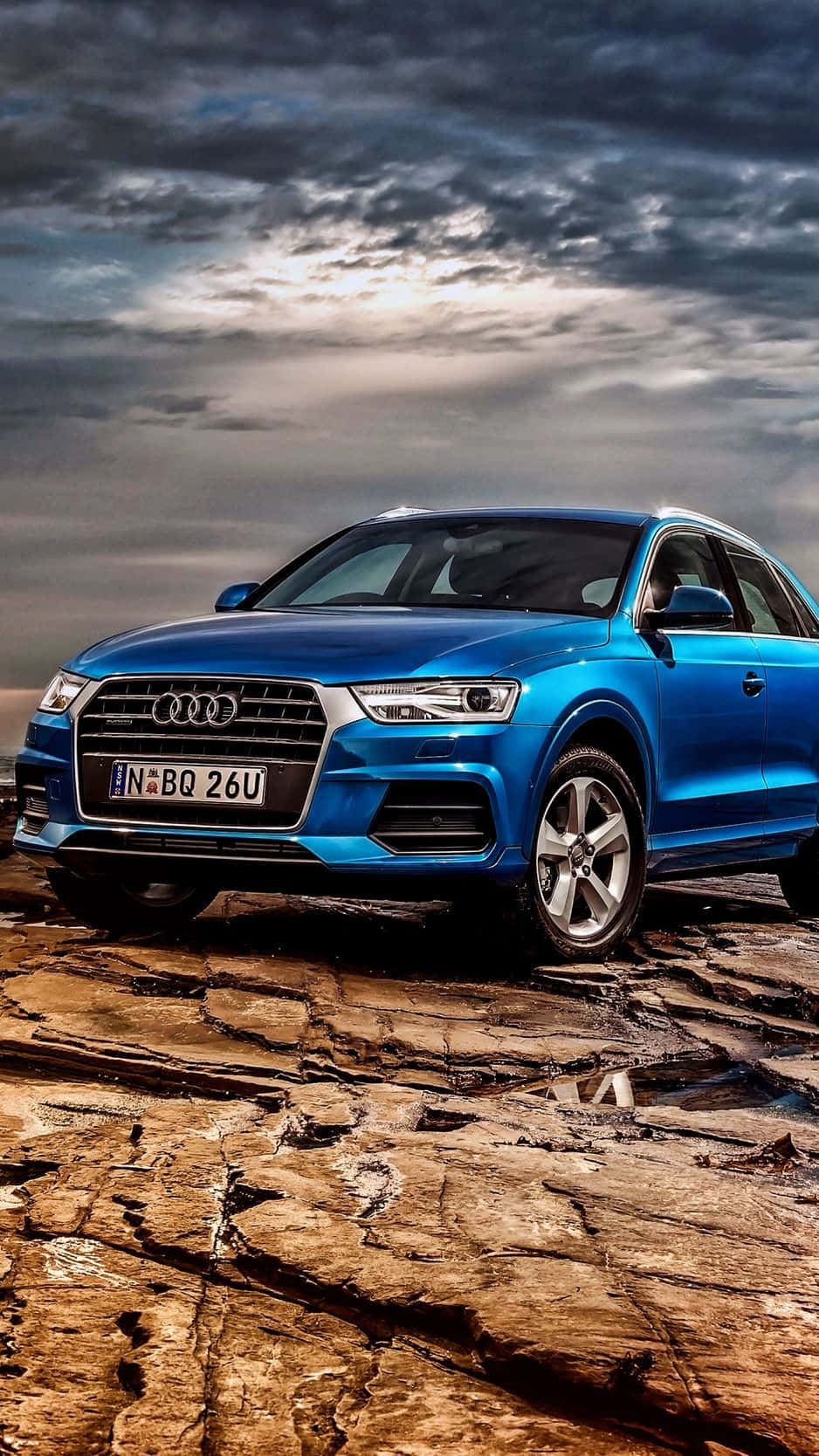 Audi Q5 桌布 壁紙 — 一輛充滿活力的藍色奧迪SUV在戲劇性的多雲天空下，矗立在堅硬、龜裂的土地上。