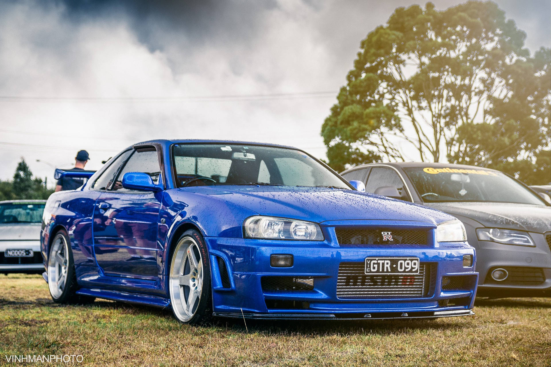 藍色日產GTR在車展中停泊在草地上，天空多雲。 — 日產 Skyline GTR R34 壁紙