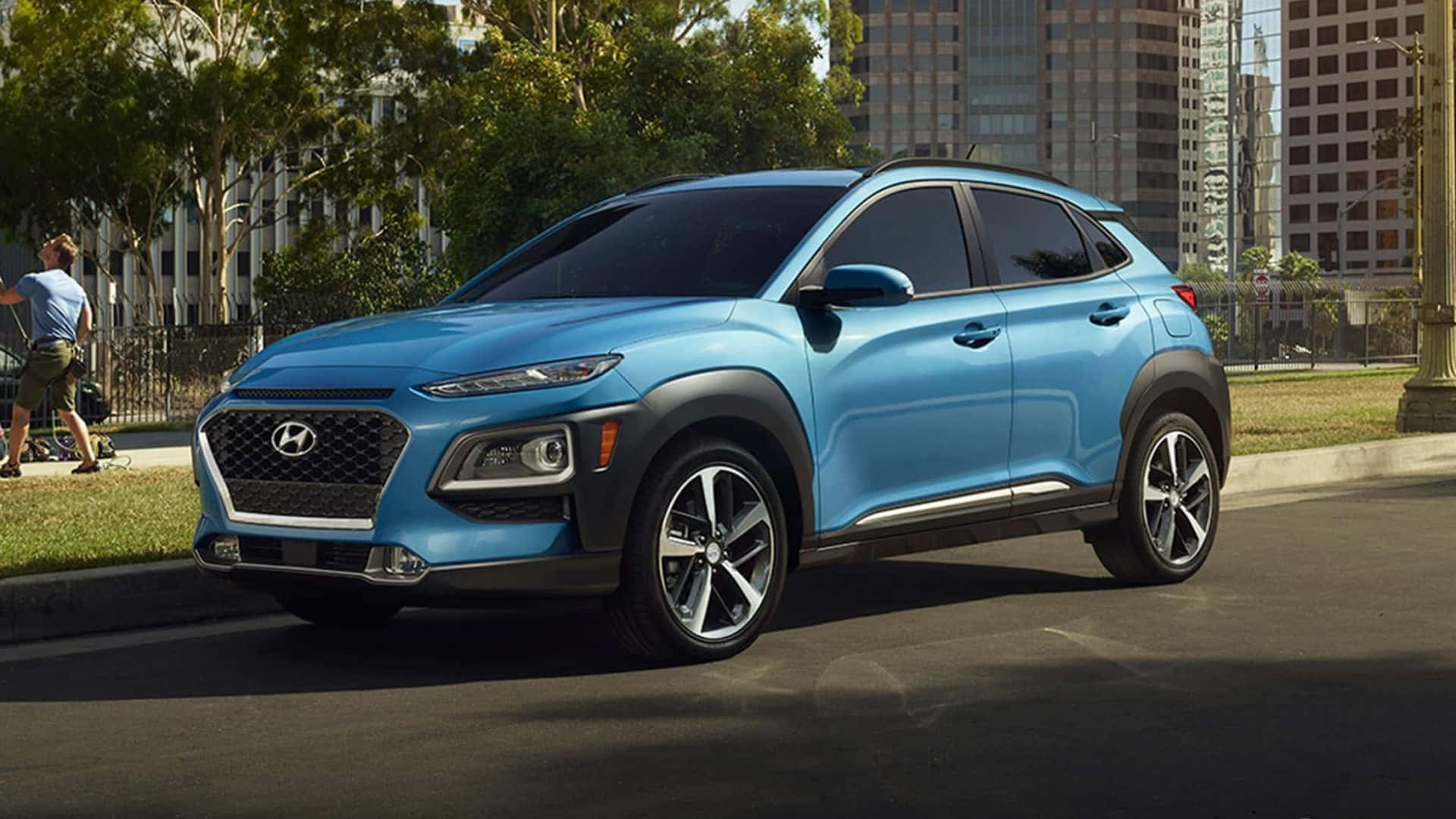 Hyundai Kona 桌布 壁紙 — 一輛充滿活力的藍色現代Kona SUV停泊在城市的街道上，背景是高樓大廈和綠樹。