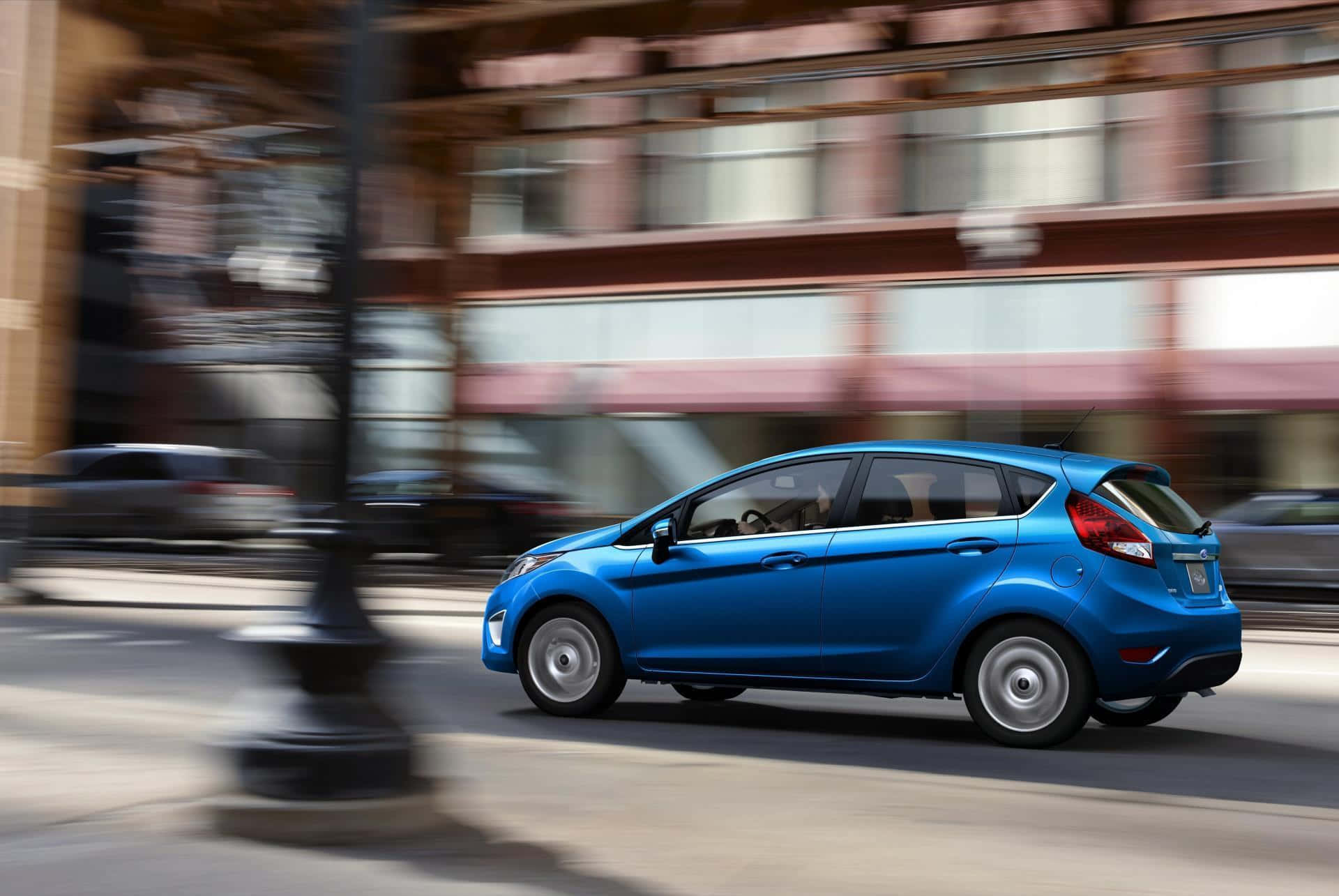 Ford Fiesta 桌布 壁紙 — 一輛充滿活力的藍色小型汽車在模糊的城市街道上疾馳，動態模糊強調了其快速移動。