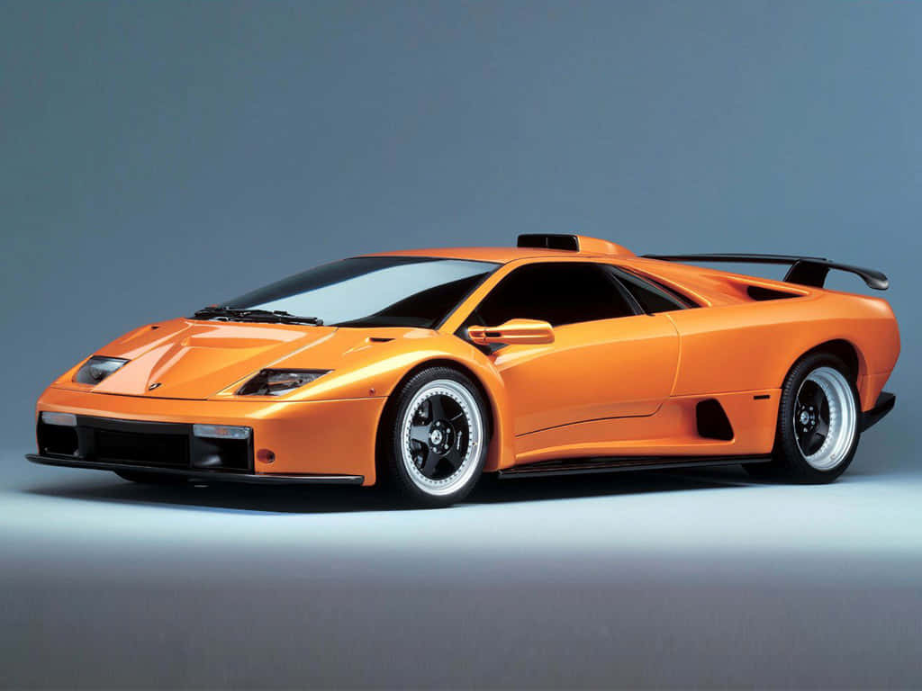 Lamborghini Diablo 桌布 壁紙 — 一輛充滿活力的橙色藍寶堅尼 Diablo SV 跑車，帶有黑色飾邊和銀色輪圈，在灰色漸變工作室背景前擺拍。