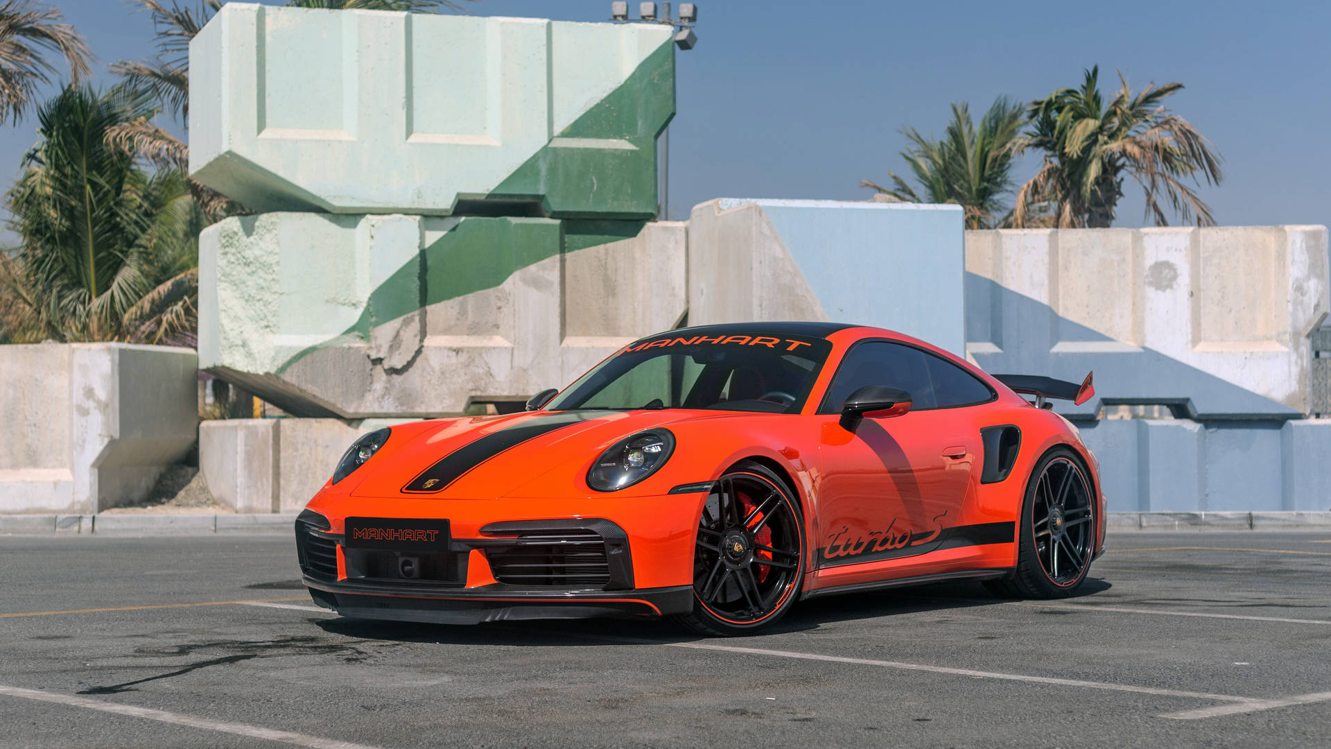 橙色Manhart保時捷911 Turbo S停泊在混凝土塊和棕櫚樹附近。 — 4K 壁紙
