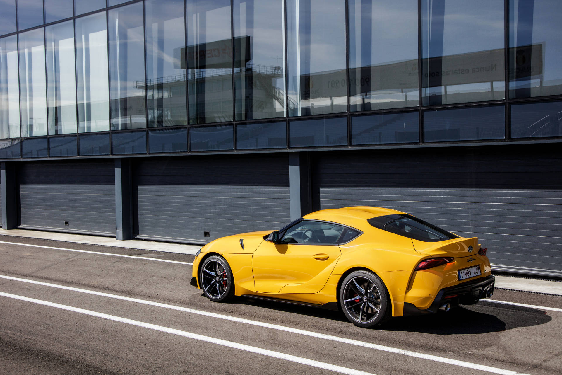 黃色跑車停泊在玻璃建築旁的瀝青停車場上。 — Toyota Supra 壁紙
