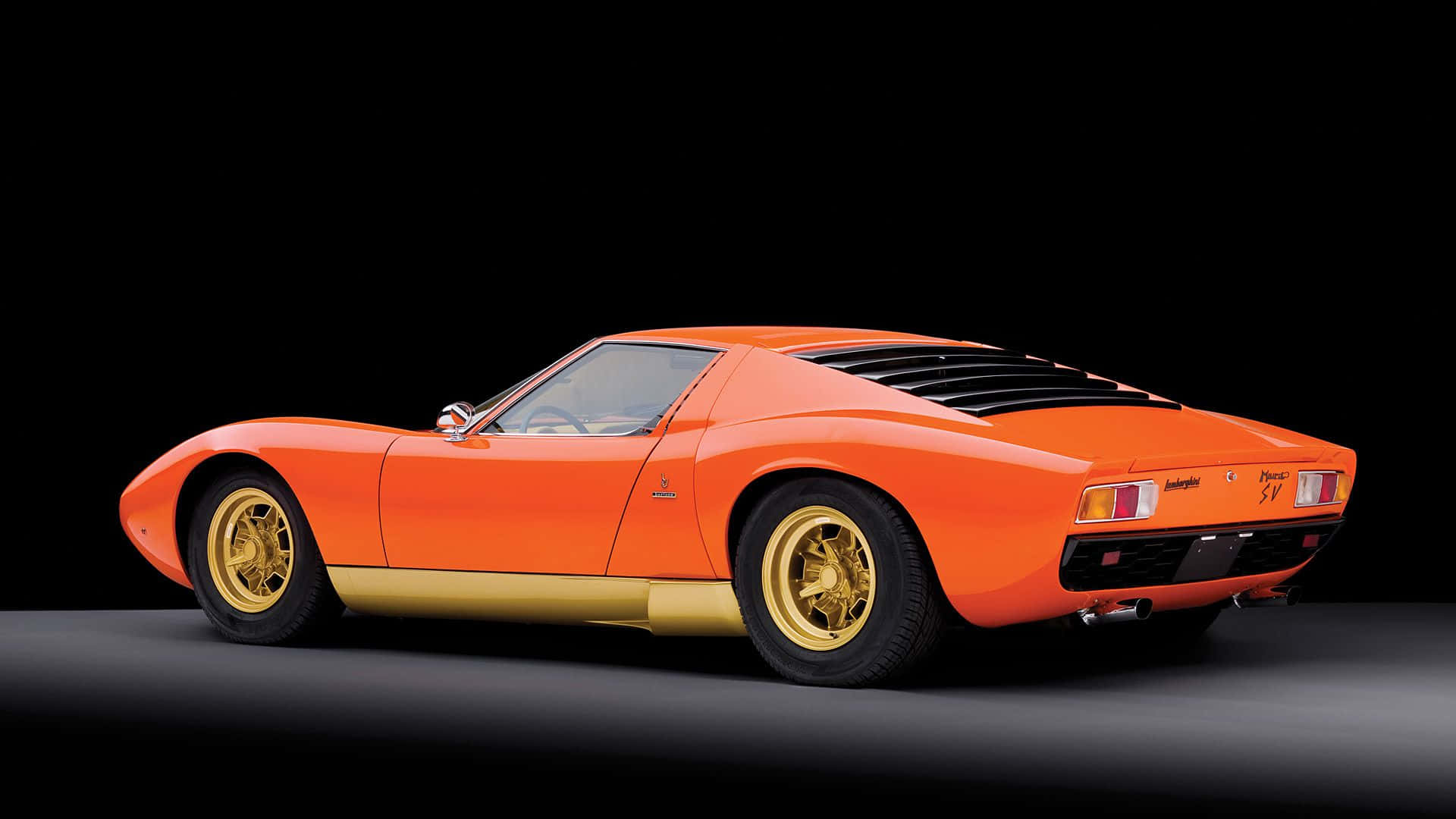 Lamborghini Miura 桌布 壁紙 — 一輛充滿活力的橘色藍寶堅尼Miura跑車，配備金色飾件和輪圈，在黑色背景的攝影棚中展示。