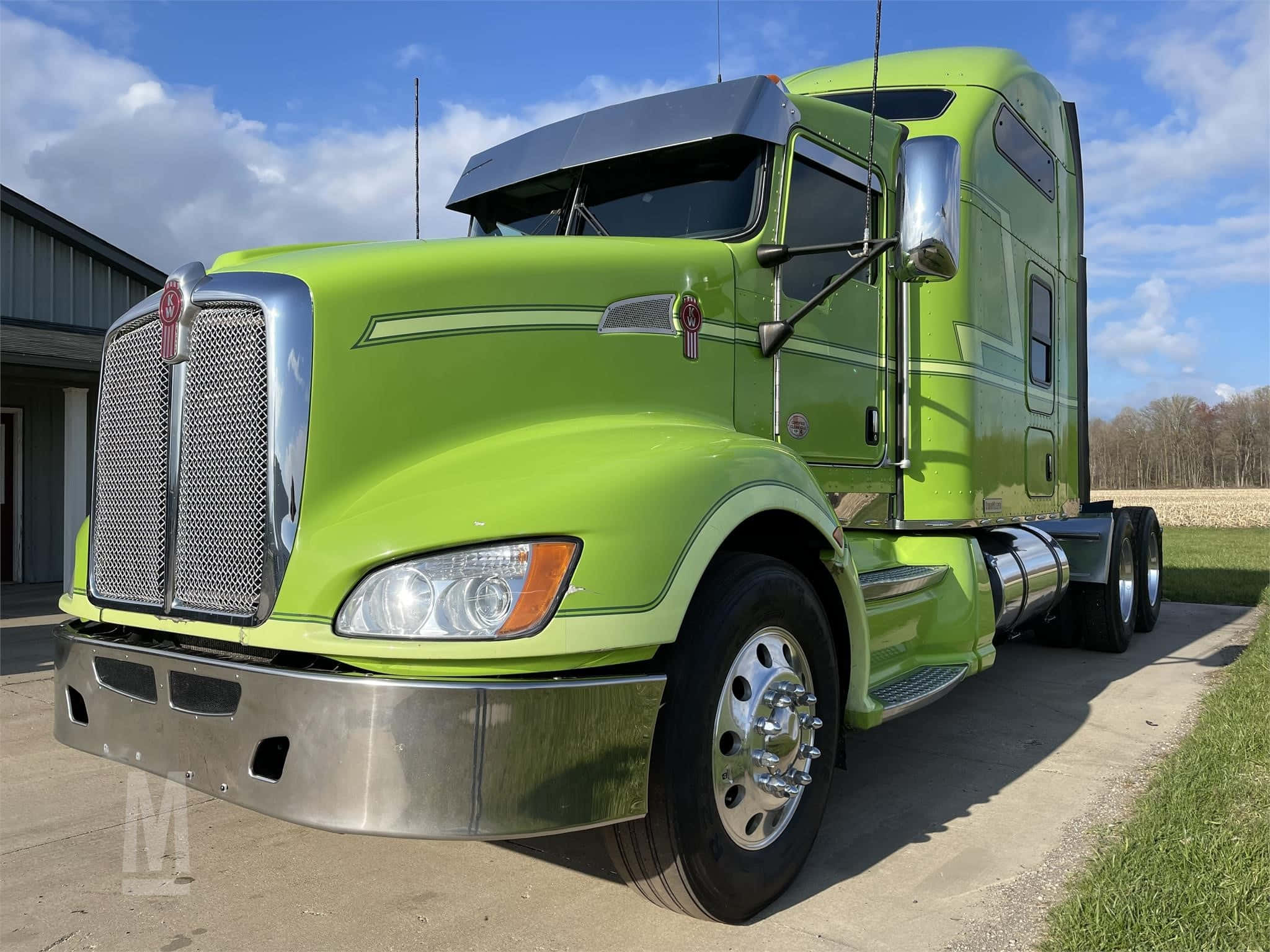 Kenworth T660 桌布 壁紙 — 一輛充滿活力的萊姆綠色半掛卡車，帶有鍍鉻裝飾，停在混凝土墊上，旁邊是草地，天空部分多雲。