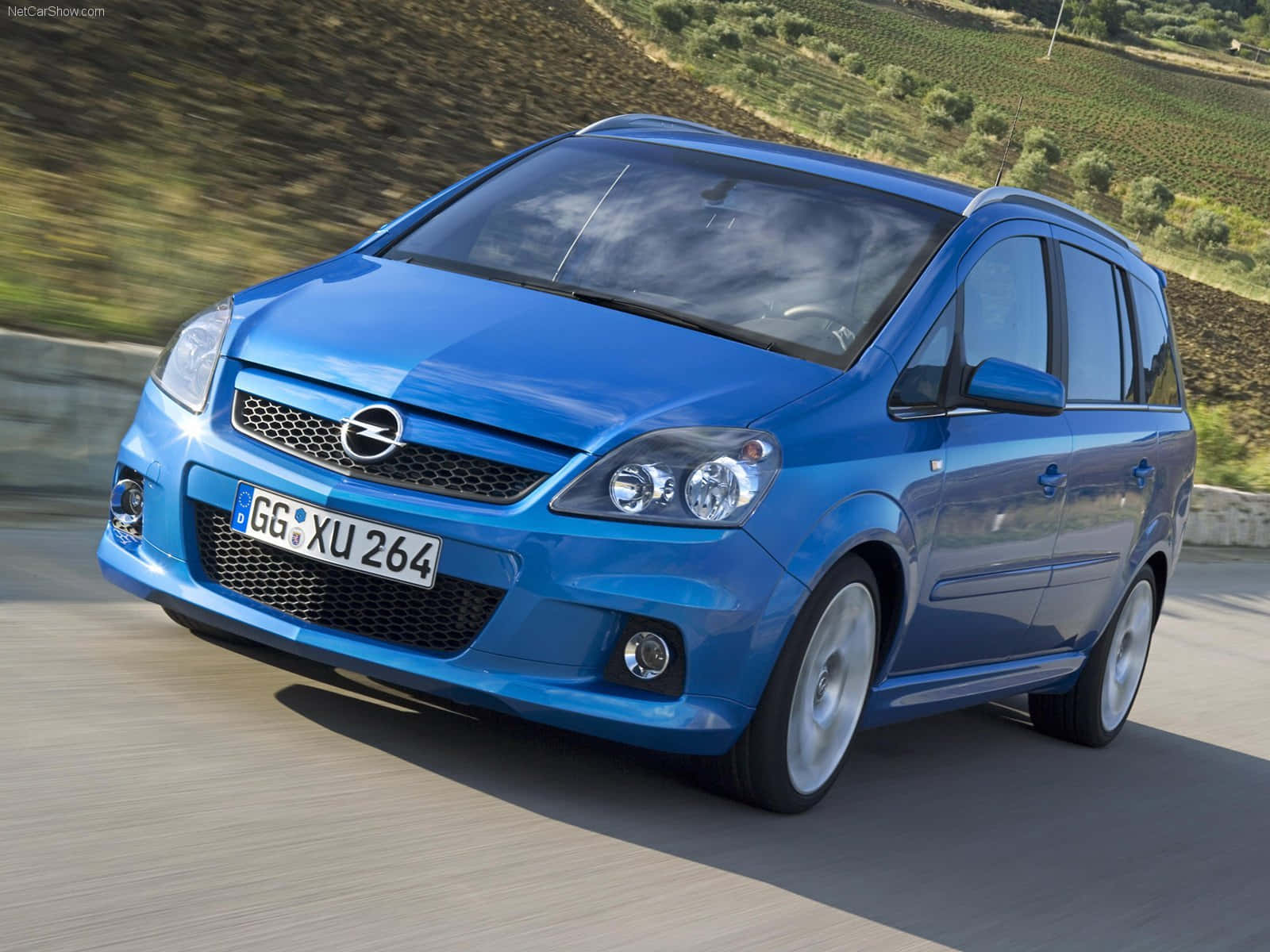 Opel Zafira 桌布 壁紙 — 一輛充滿活力的藍色歐寶Zafira在陽光明媚的起伏山丘間的蜿蜒道路上疾馳，帶有模糊的動感。