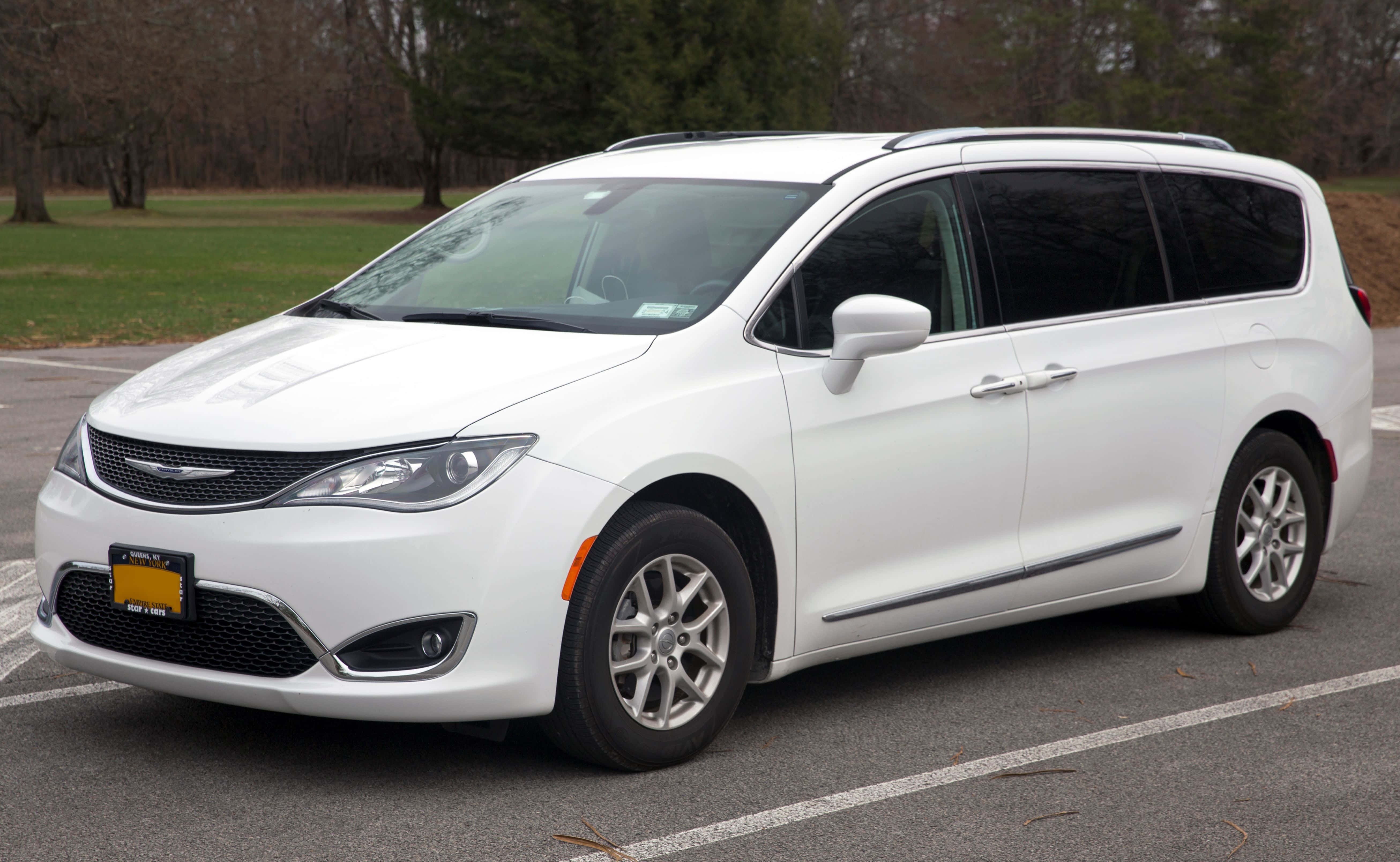 Chrysler Pacifica 桌布 壁紙 — 一輛純白色的 Chrysler Pacifica 小型貨車停放在瀝青停車場，背景有光禿的樹木和草地。