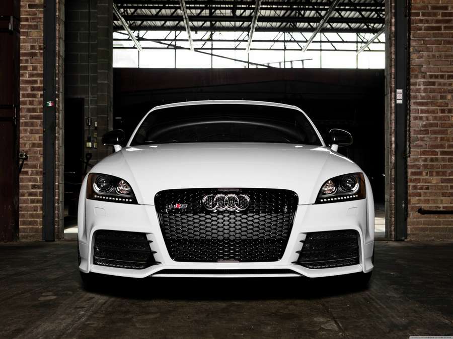 Audi Tt Rs 桌布 壁紙 — 一輛純白色的奧迪TT RS跑車停放在一個質樸的磚砌車庫中央，車庫擁有高聳的工業風天花板。