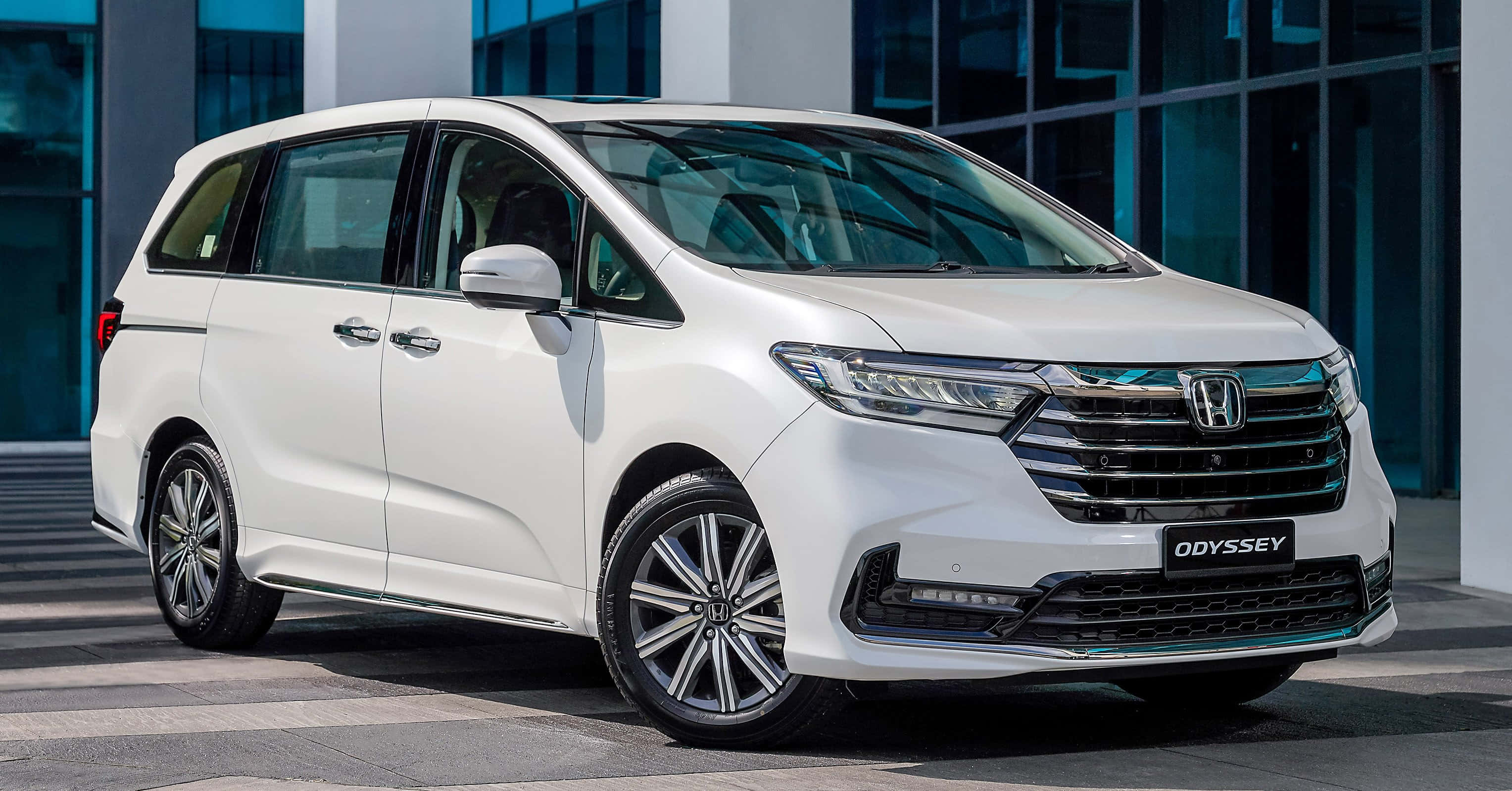 Honda Odyssey 桌布 壁紙 — 一輛純白色的本田Odyssey廂型車停在現代玻璃建築前，在明亮的日光下。