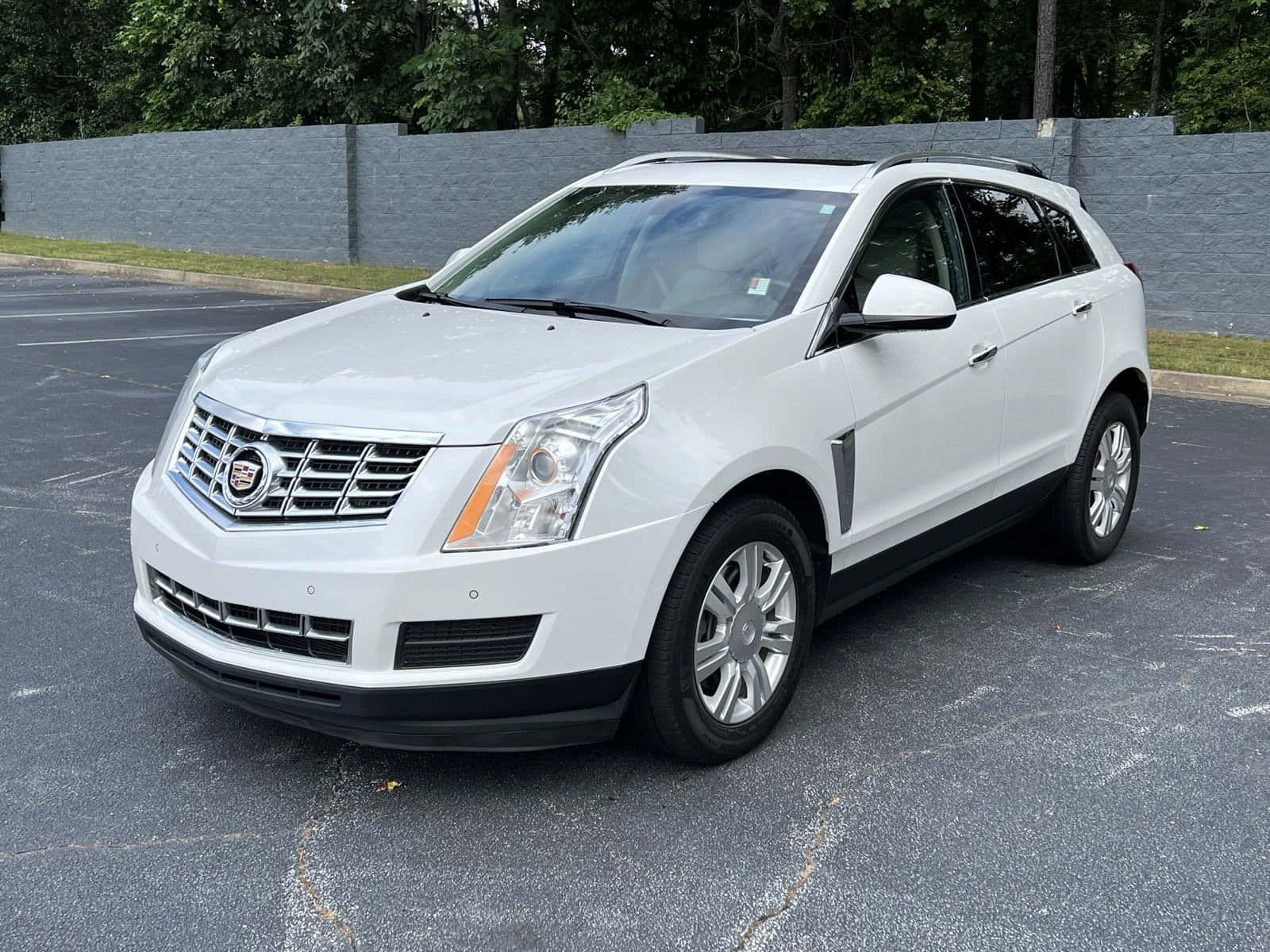 Cadillac Srx 桌布 壁紙 — 一輛純白色的 Cadillac SRX SUV 停放在瀝青停車場，背景有樹木和灰色牆壁。