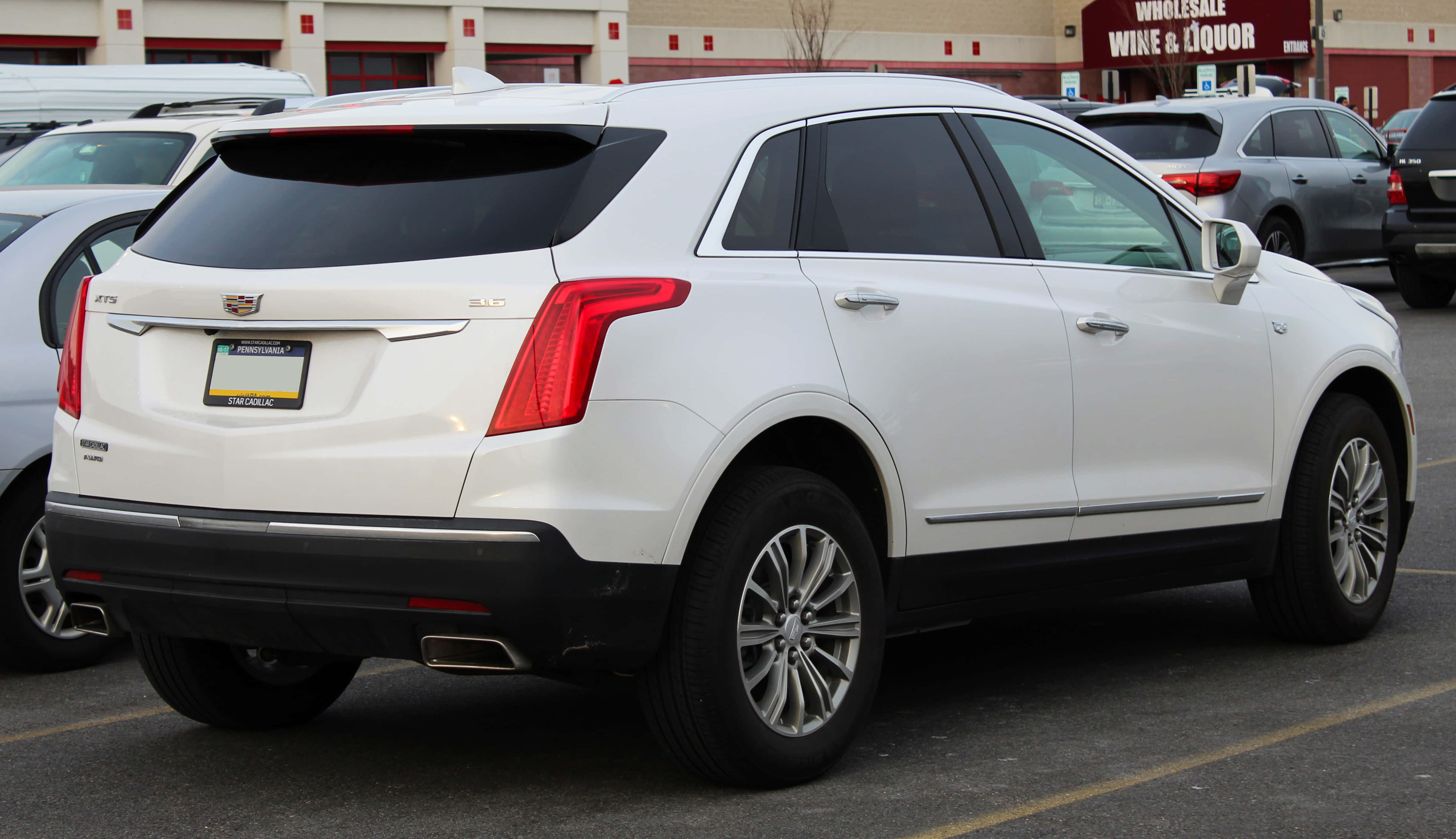 Cadillac Xt5 桌布 壁紙 — 一輛純白色的Cadillac XT5 SUV停放在商業停車場，背景有其他車輛和一間批發酒類商店。