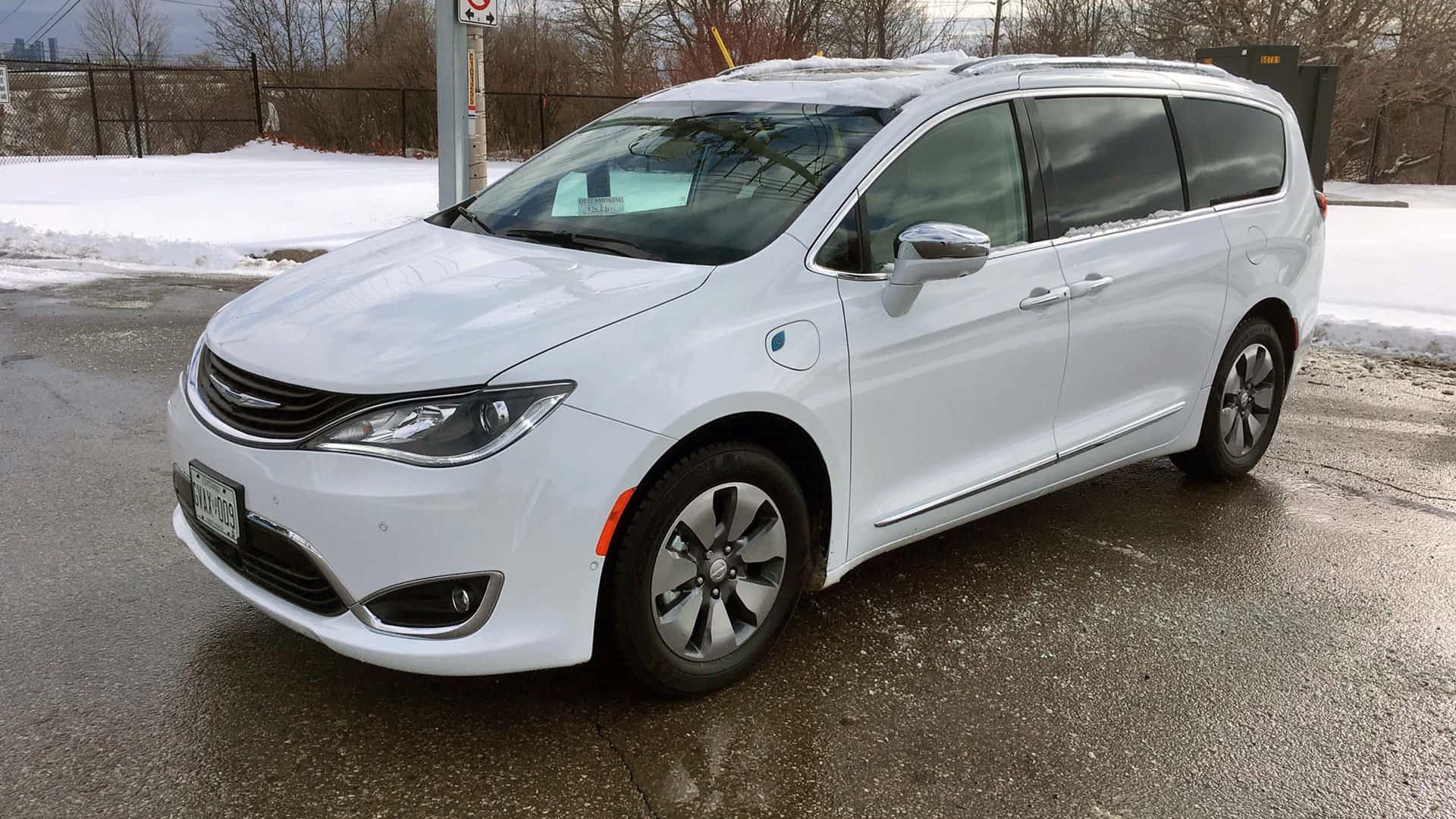 Chrysler Pacifica 桌布 壁紙 — 一輛純白色的 Chrysler Pacifica Hybrid 小型貨車停放在濕漉漉的瀝青停車場上，背景有積雪。