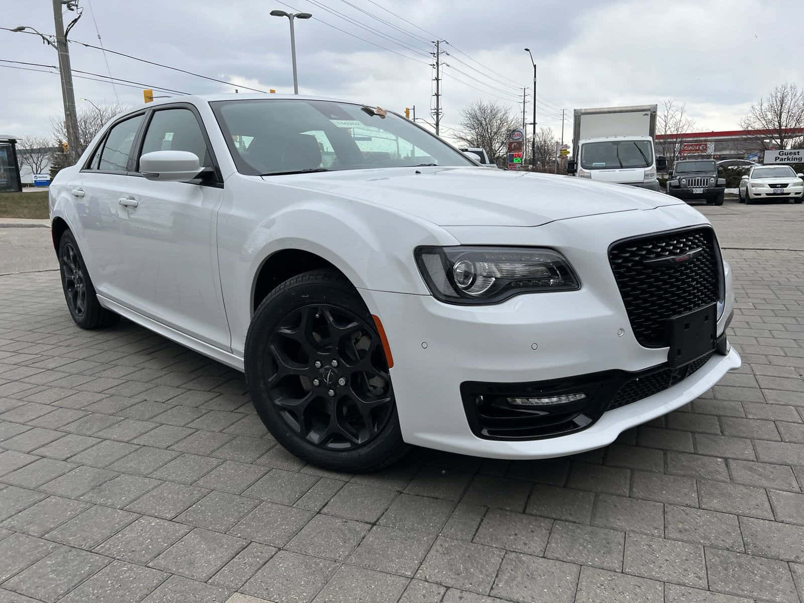 Chrysler 300 桌布 壁紙 — 一輛純白色的克萊斯勒300轎車搭配黑色輪圈，停放在灰色磚地上，天空多雲。
