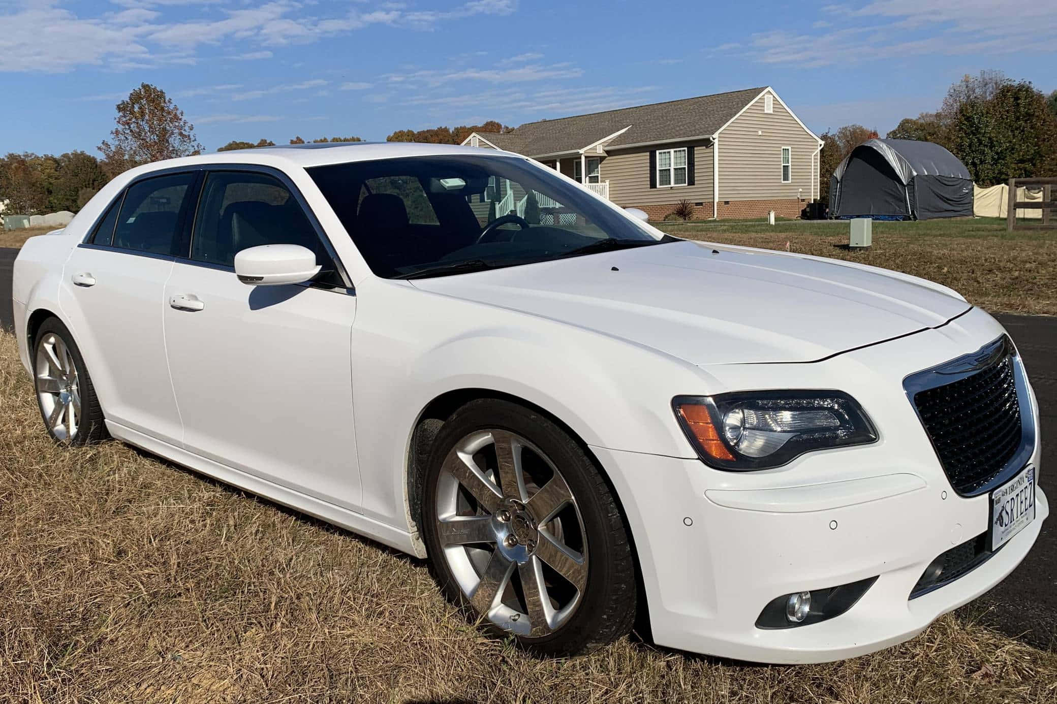 Chrysler 300 桌布 壁紙 — 一輛純白色的克萊斯勒轎車停在乾草地上，背景是晴朗的藍天和郊區房屋。