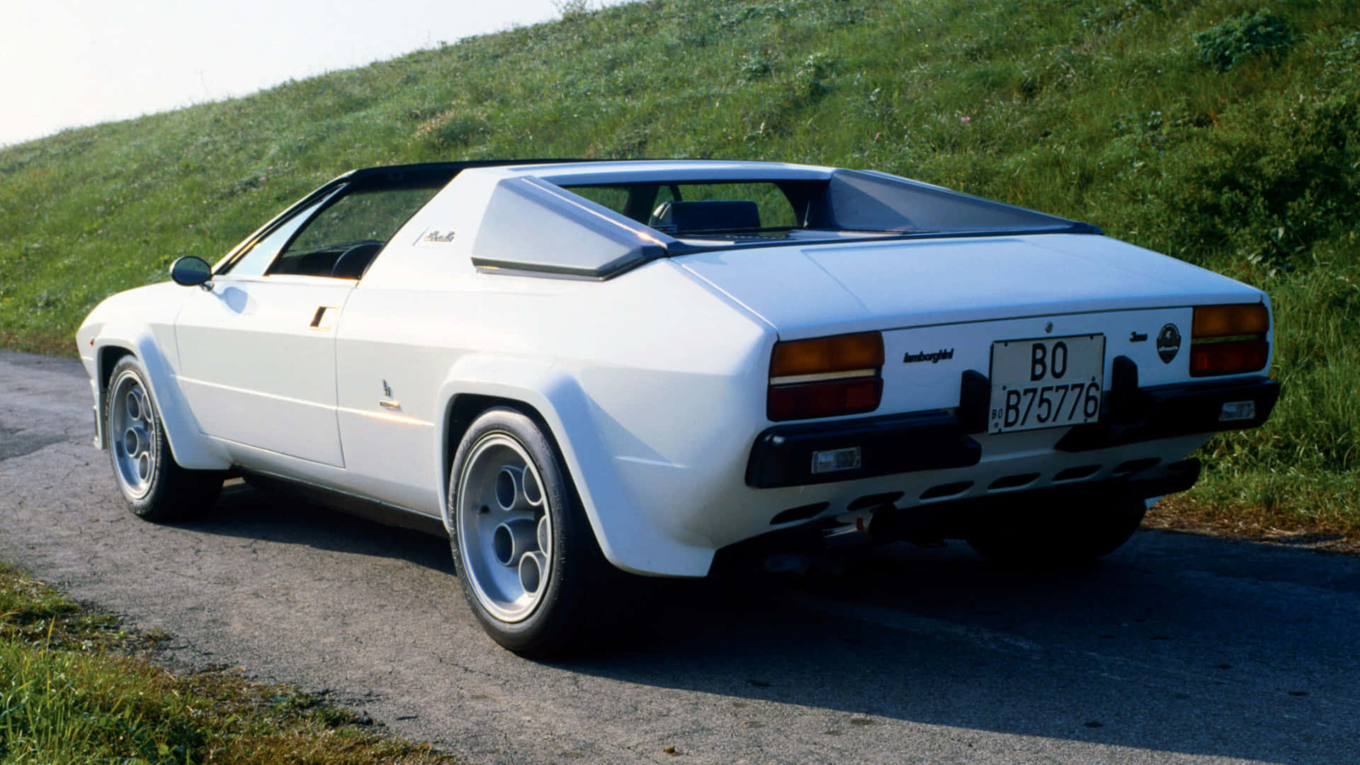 Lamborghini Silhouette 桌布 壁紙 — 一輛純白色的藍寶堅尼 Jalpa 跑車停泊在碎石路上，旁邊是長滿青草的山丘，在明亮的日光下。