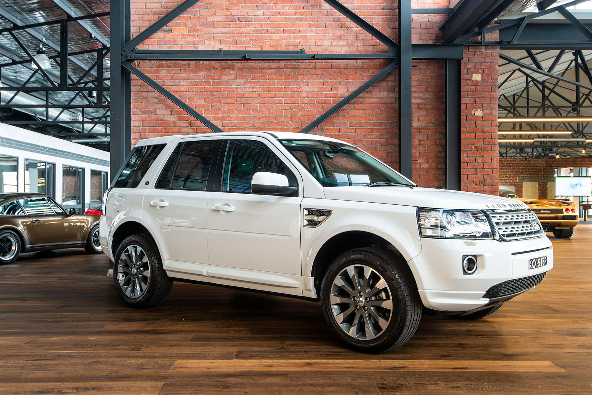 Land Rover Freelander 桌布 壁紙 — 一輛純白色的 Land Rover Freelander II 在寬敞的磚牆汽車展廳內，在明亮的燈光下閃閃發光，地板是硬木地板。