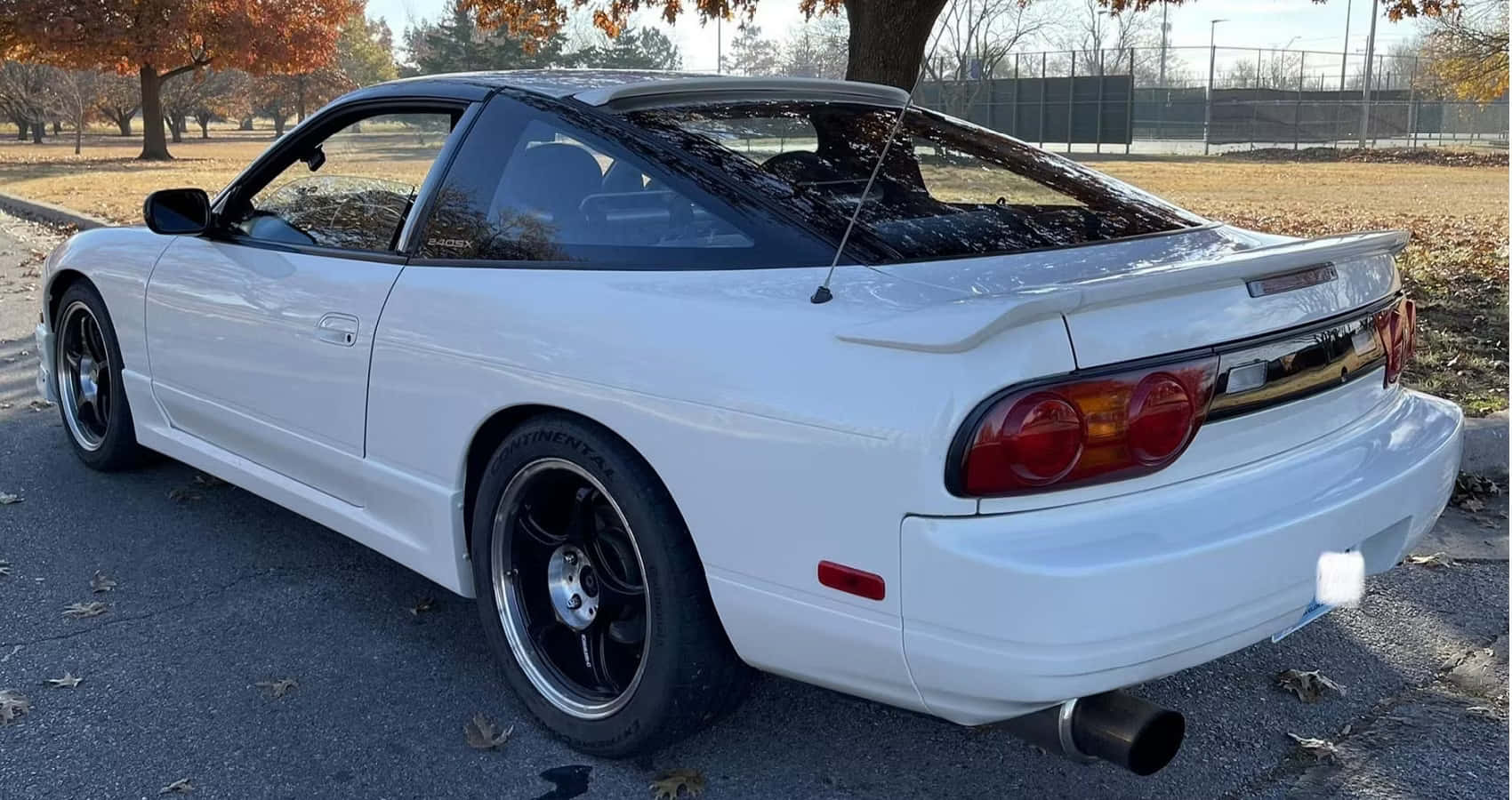  壁紙 — 一輛純白色的日產Skyline R33 GT-R停放在落葉滿佈的瀝青停車場，背景是秋天的樹木。