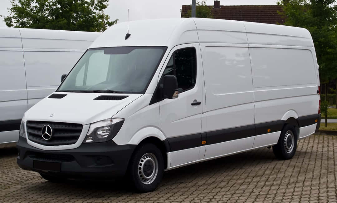 Mercedes Benz Sprinter 桌布 壁紙 — 一輛純白色的Mercedes-Benz Sprinter廂型車停放在鋪砌的停車場，背景有樹木和另一輛廂型車。