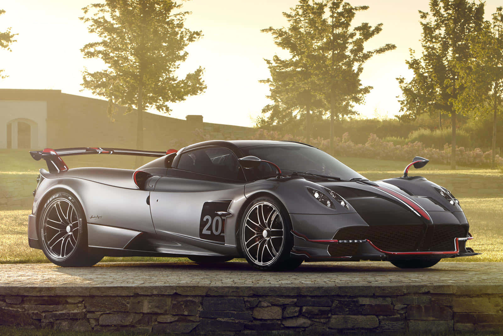 Pagani Huayra Roadster Bc 桌布 壁紙 — 一輛帶有紅色點綴的時尚銀色帕加尼 Huayra 跑車在黃金時段停放在石牆上。
