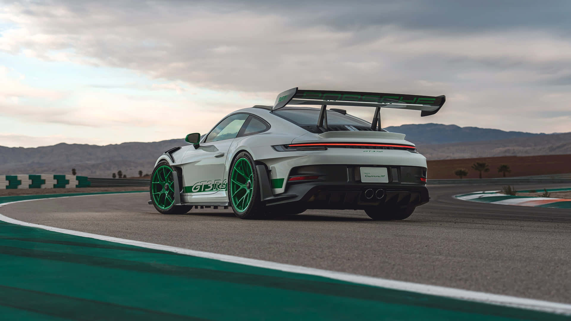  壁紙 — 一輛帶有綠色點綴的白色保時捷911 GT3 RS在陰天下的沙漠賽道上奔馳。