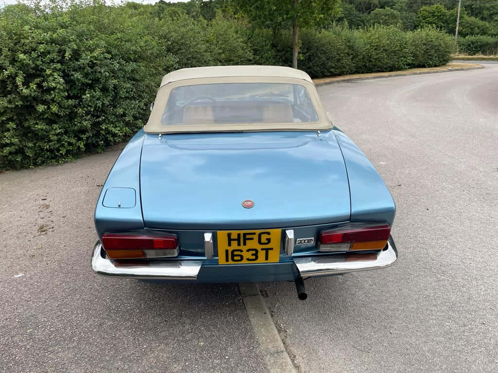 Fiat 124 Spider 桌布 壁紙 — 一輛復古淺藍色Fiat 124 Spider敞篷車停在柏油路上，背景有綠色樹籬。