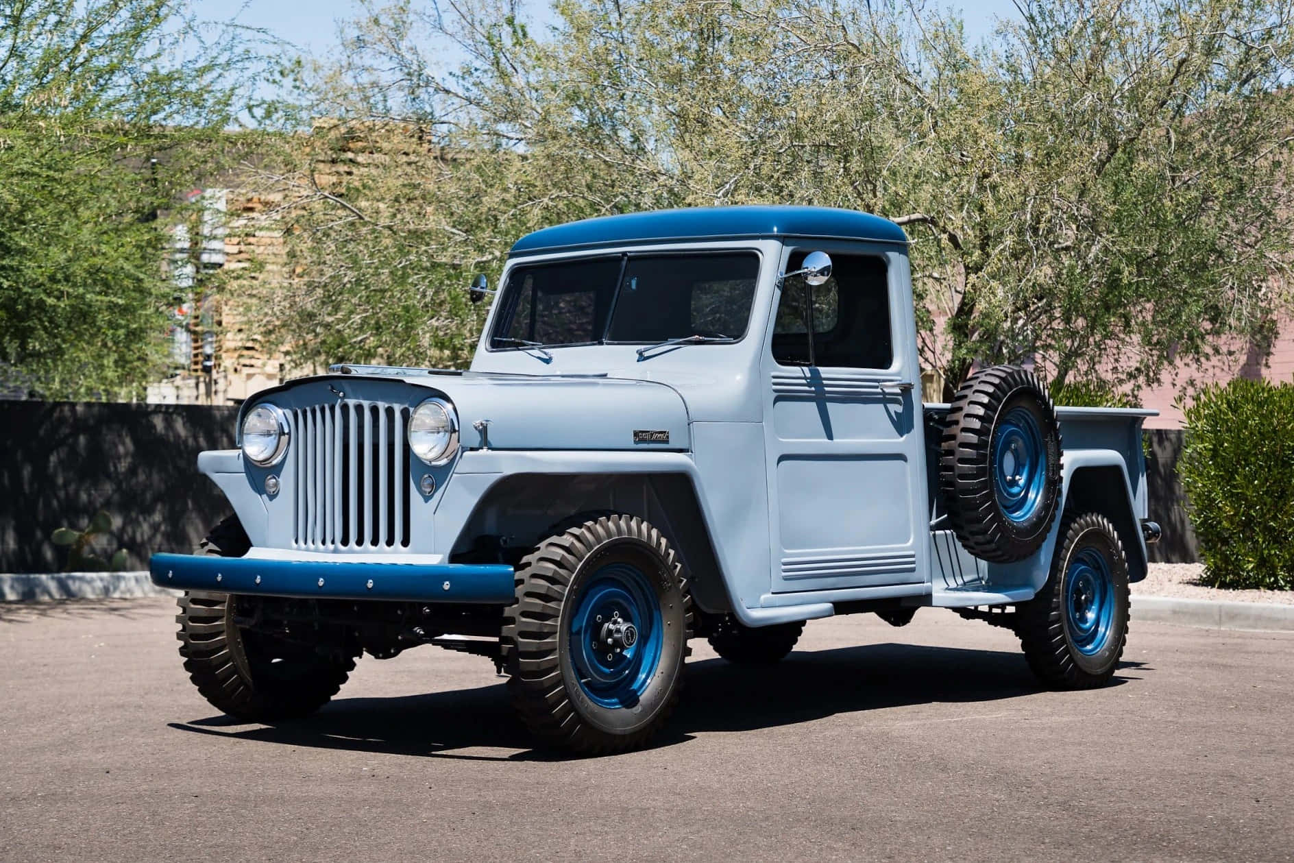Jeep Willys 桌布 壁紙 — 一輛復古淺藍色和深藍色Jeep皮卡車，側面裝有備用輪胎，停在陽光普照的瀝青路上。