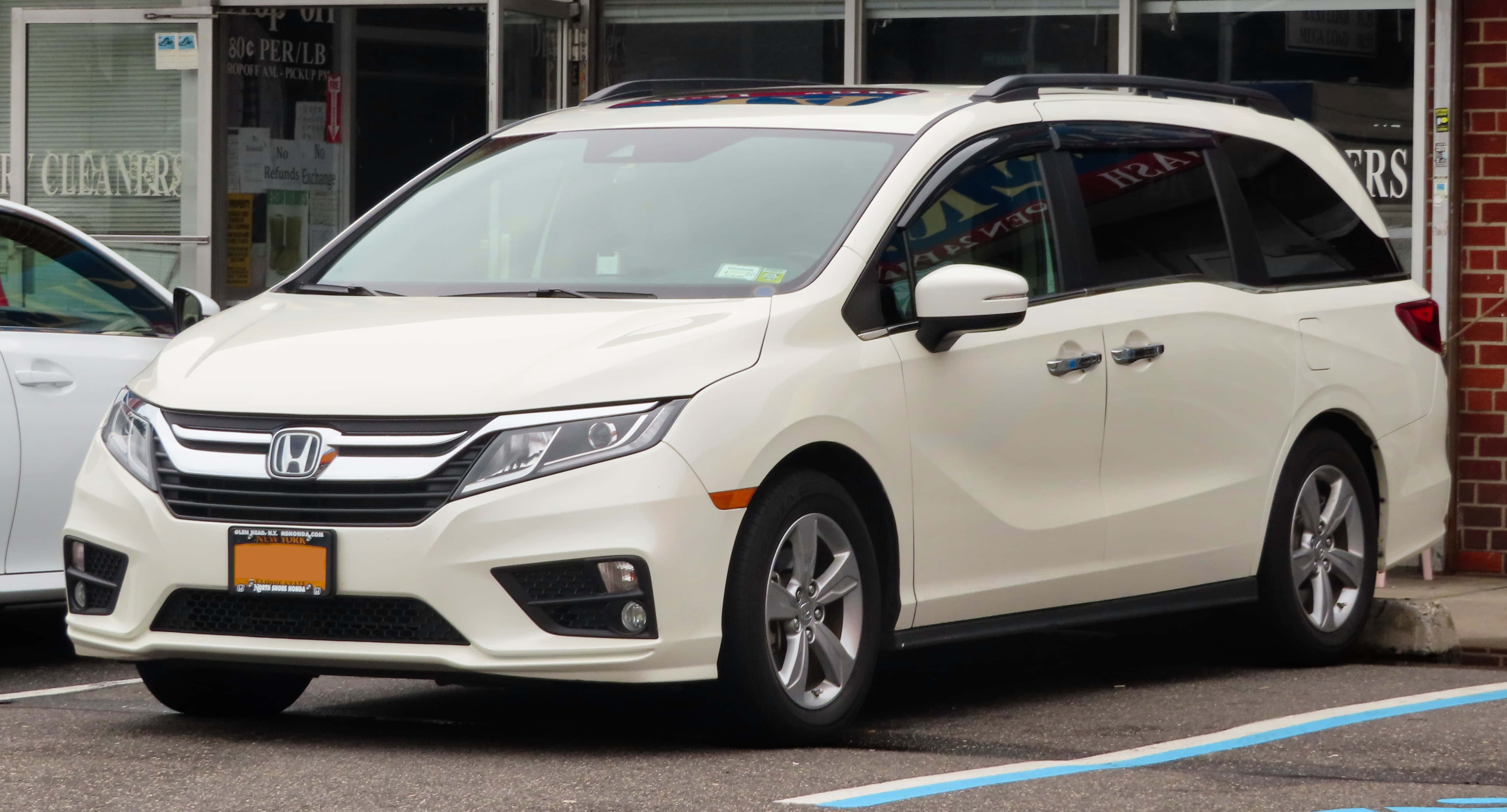 Honda Odyssey 桌布 壁紙 — 一輛乾淨的白色本田Odyssey小型貨車停放在城市空地，旁邊有一棟磚造建築和另一輛車。