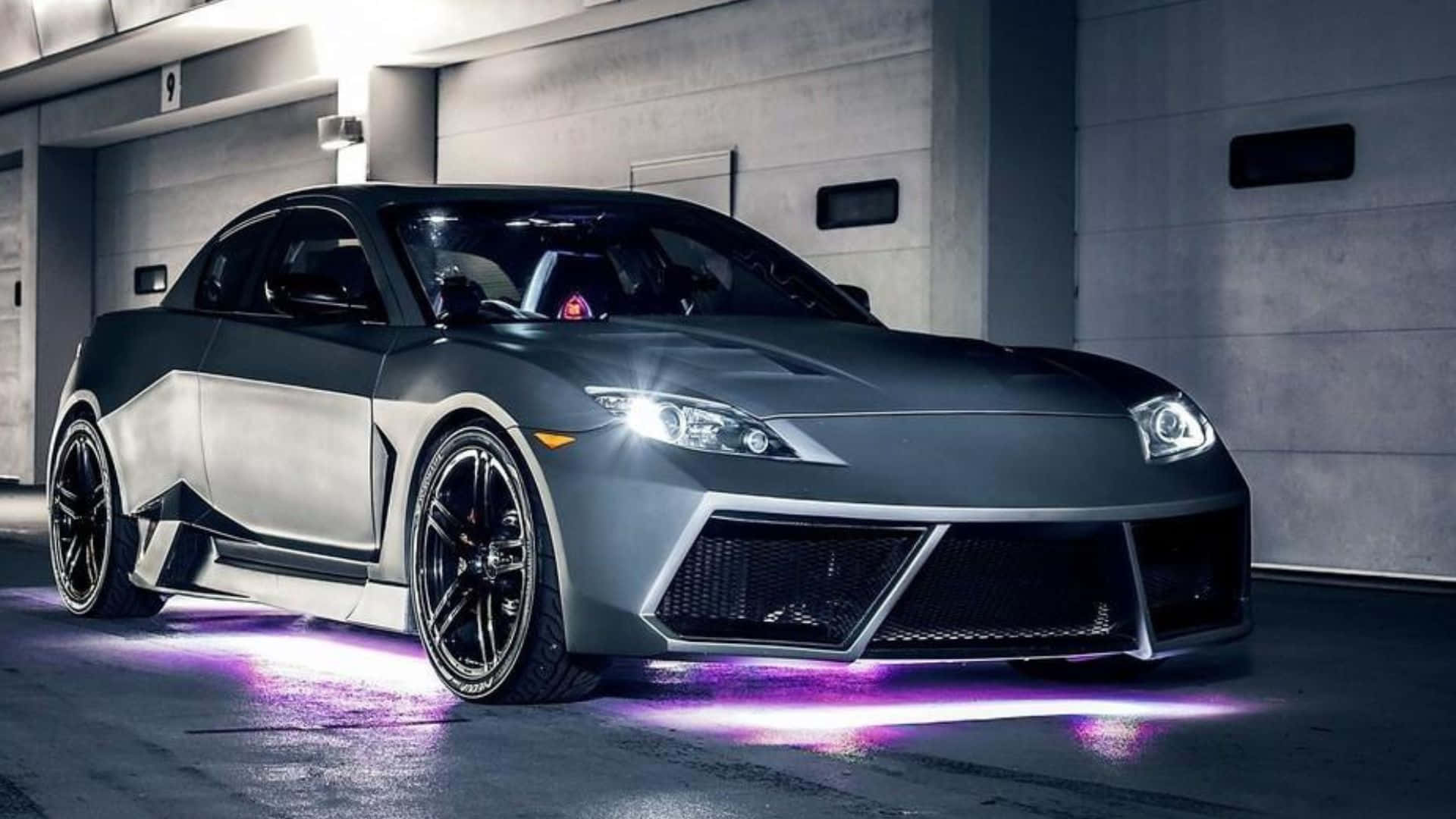 Mazda Rx-8 桌布 壁紙 — 一輛光滑的消光灰色跑車，帶有發光的紫色底盤燈，停放在昏暗的混凝土車庫中。