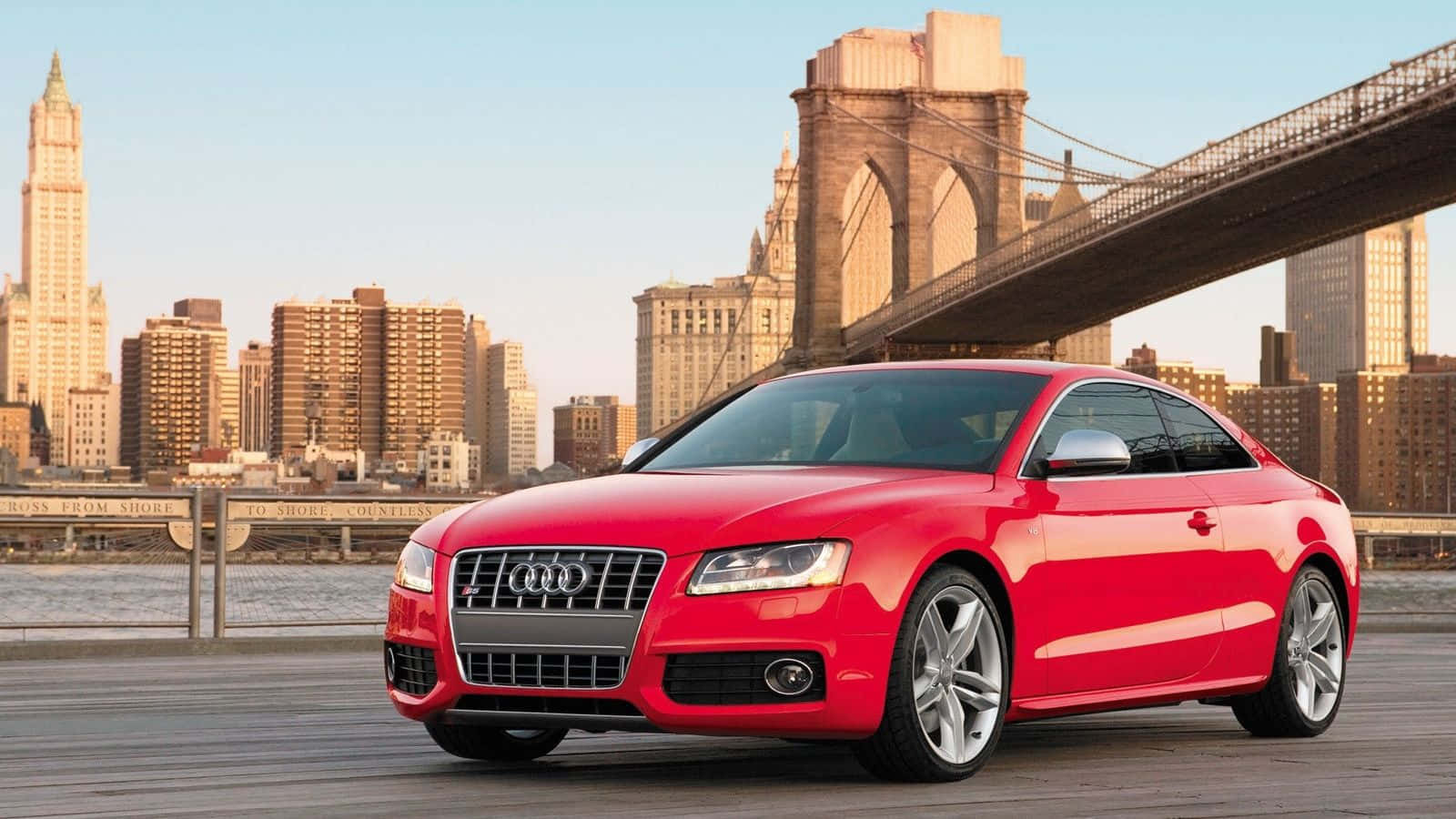 Audi S5 桌布 壁紙 — 一輛光亮的紅色奧迪雙門跑車停泊在木製碼頭上，背景是布魯克林大橋和曼哈頓天際線，正值黃金時刻。