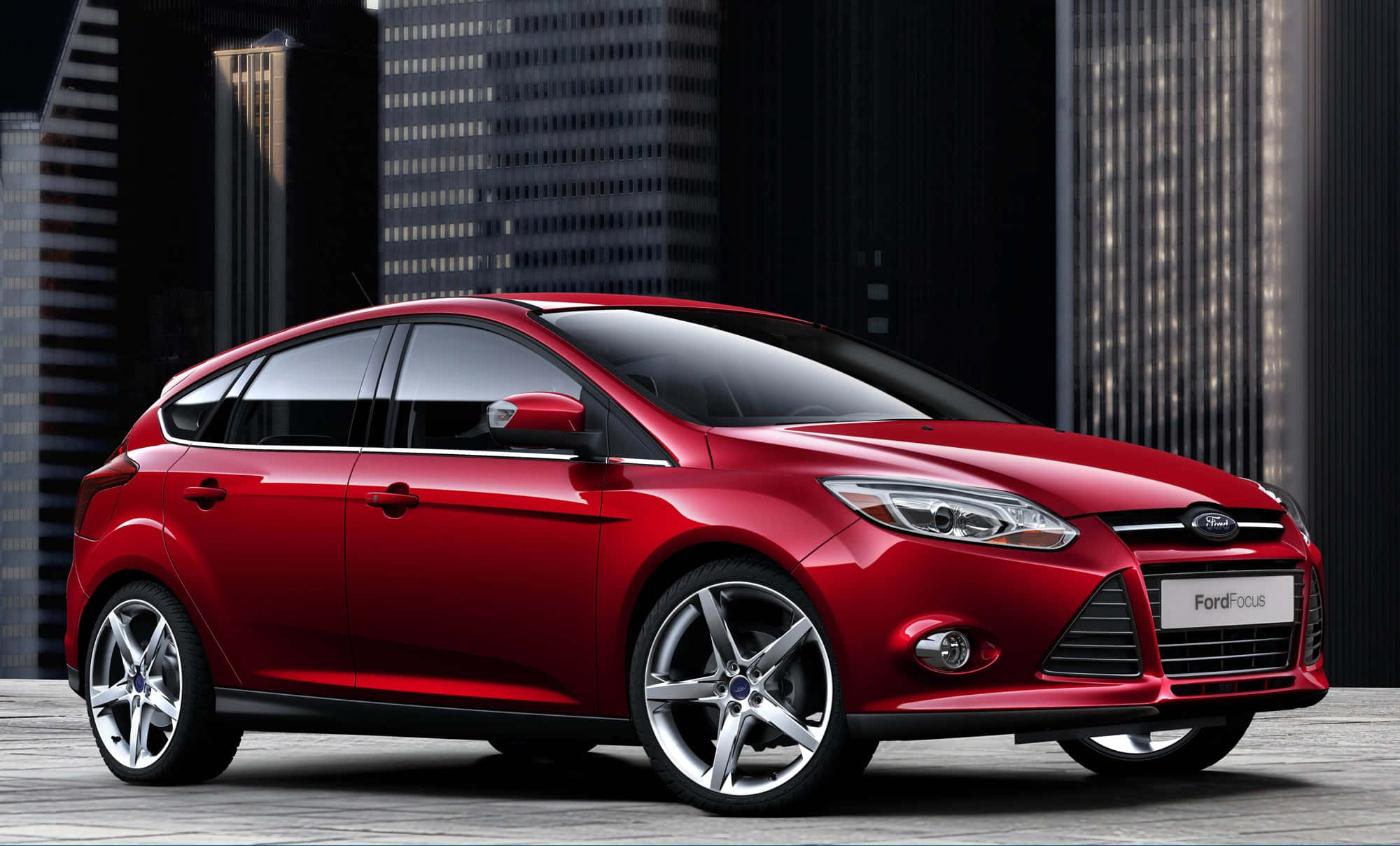 Ford Focus 桌布 壁紙 — 一輛光亮的紅色福特福克斯掀背車在明亮燈光下閃耀，背景是深色的現代摩天大樓。