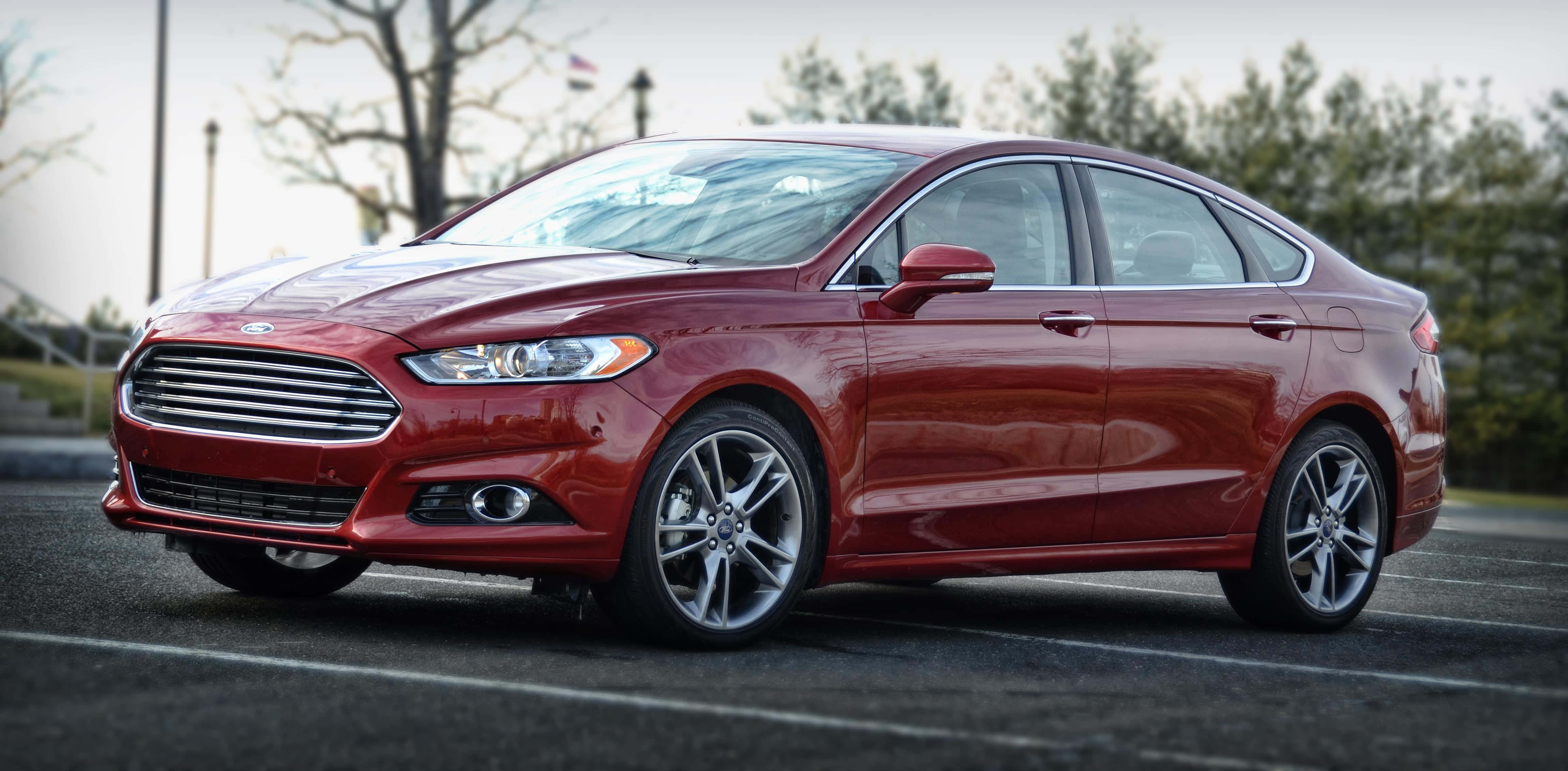 Ford Fusion 桌布 壁紙 — 一輛光亮的紅色福特Fusion房車停放在戶外停車場，背景有樹木和路燈。