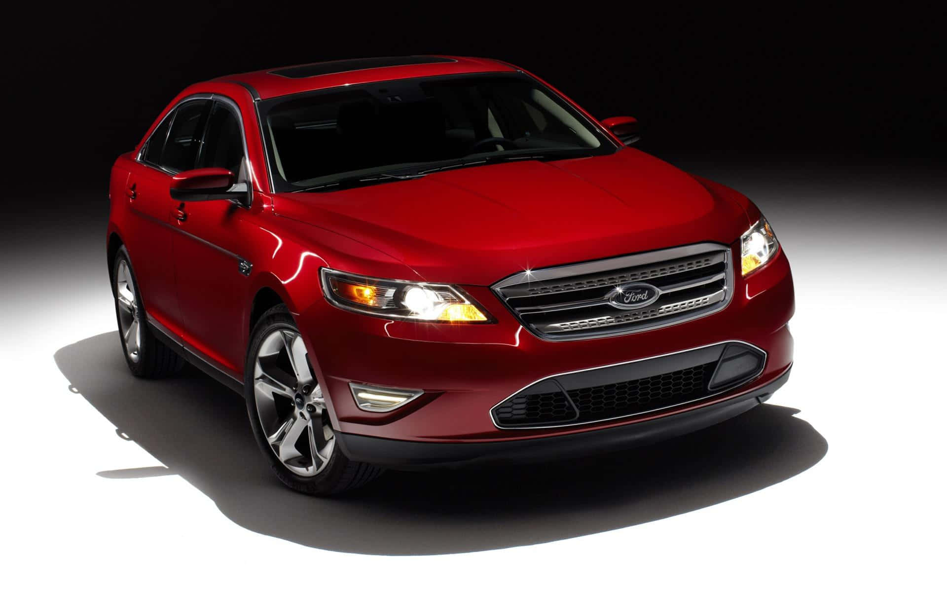 Ford Taurus 桌布 壁紙 — 一輛光亮的紅色福特轎車在攝影棚燈光下，在鮮明的黑白漸變背景上閃閃發光。