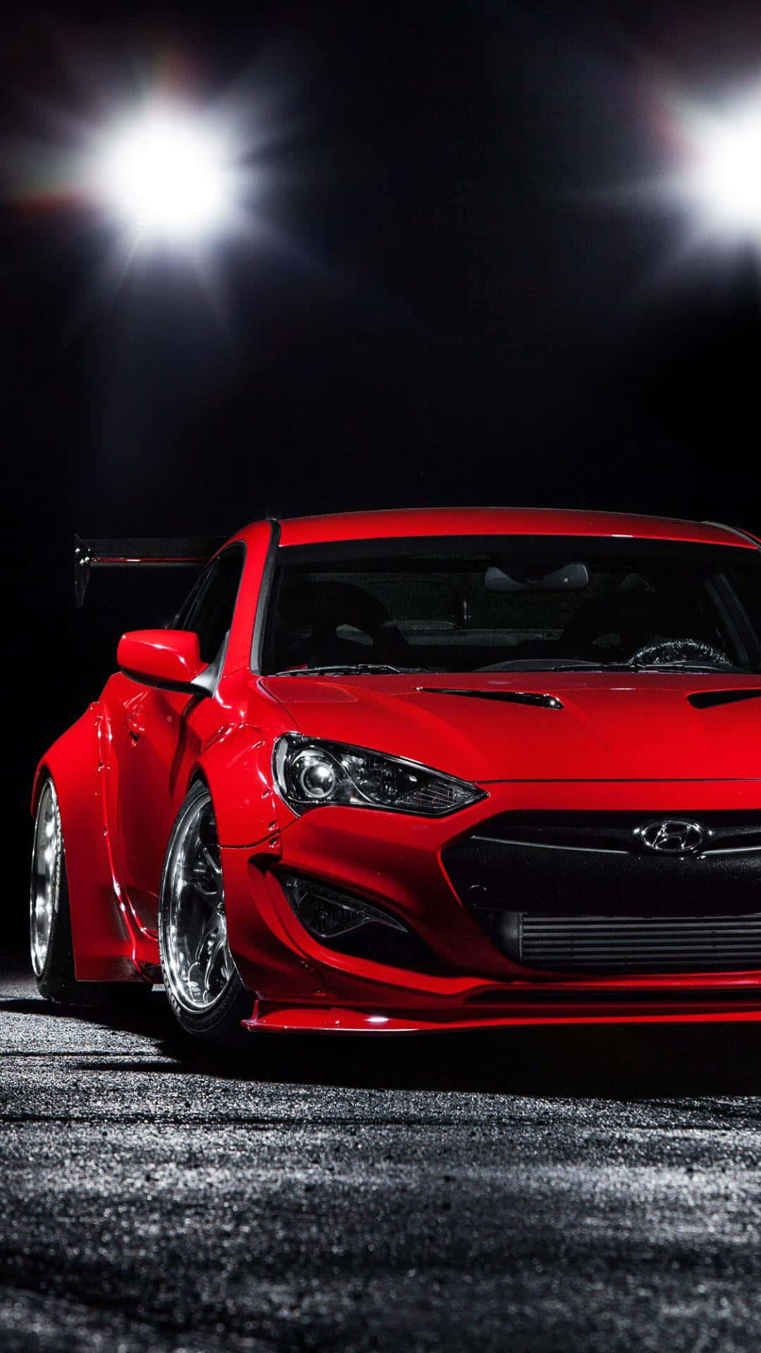 Hyundai Genesis 桌布 壁紙 — 一輛光亮的紅色改裝跑車在黑暗潮濕的瀝青路面上，在明亮的聚光燈下閃閃發光。