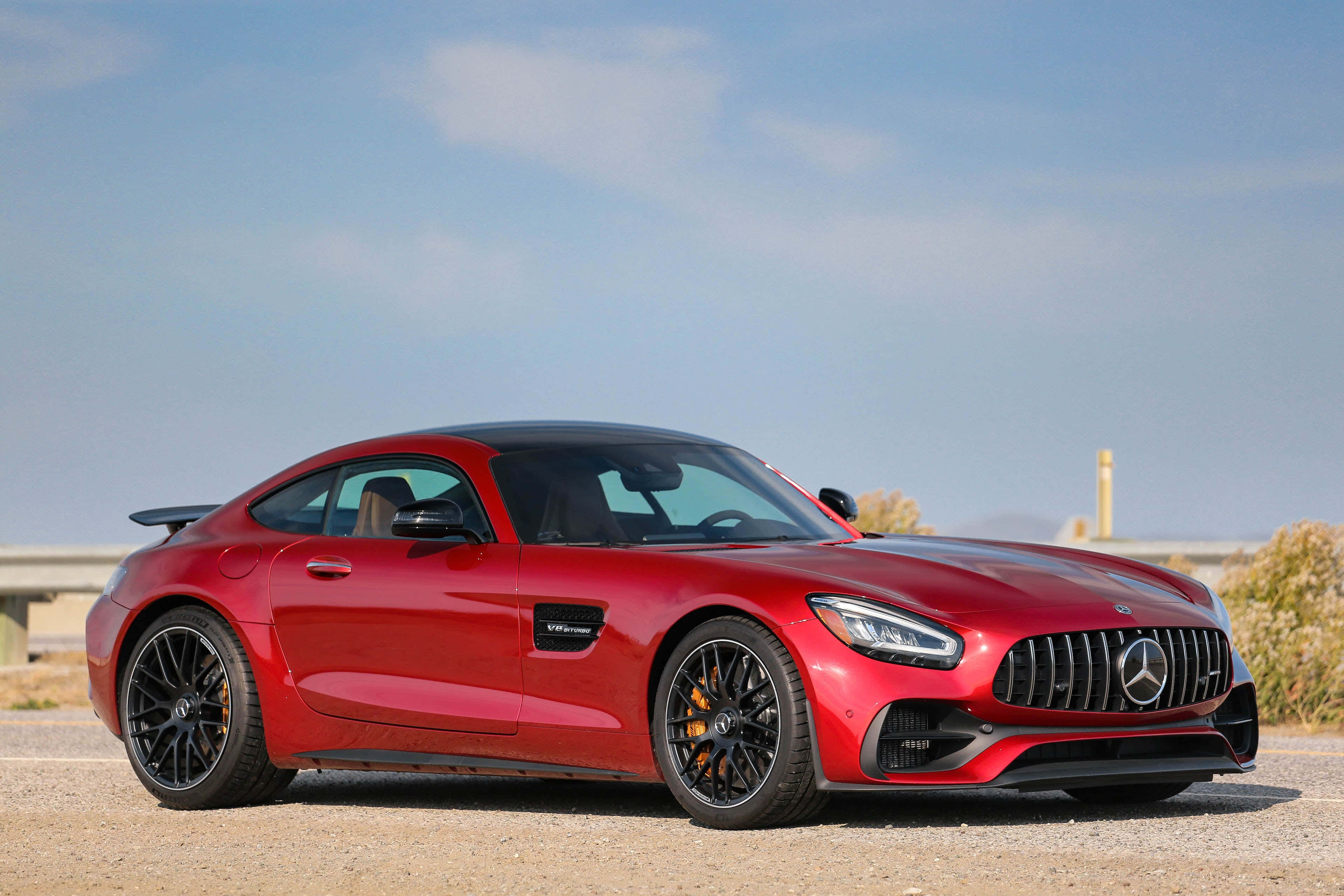 Mercedes Benz Amg Gt 桌布 壁紙 — 一輛光亮的紅色Mercedes-AMG GT R跑車停在碎石上，背景是晴朗的藍天和遠山。
