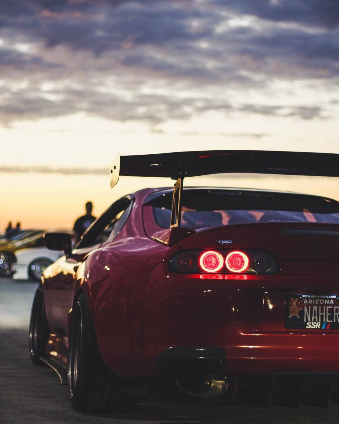 日落時分，紅色跑車車尾燈發光，背景有人群。 — Toyota Supra 壁紙