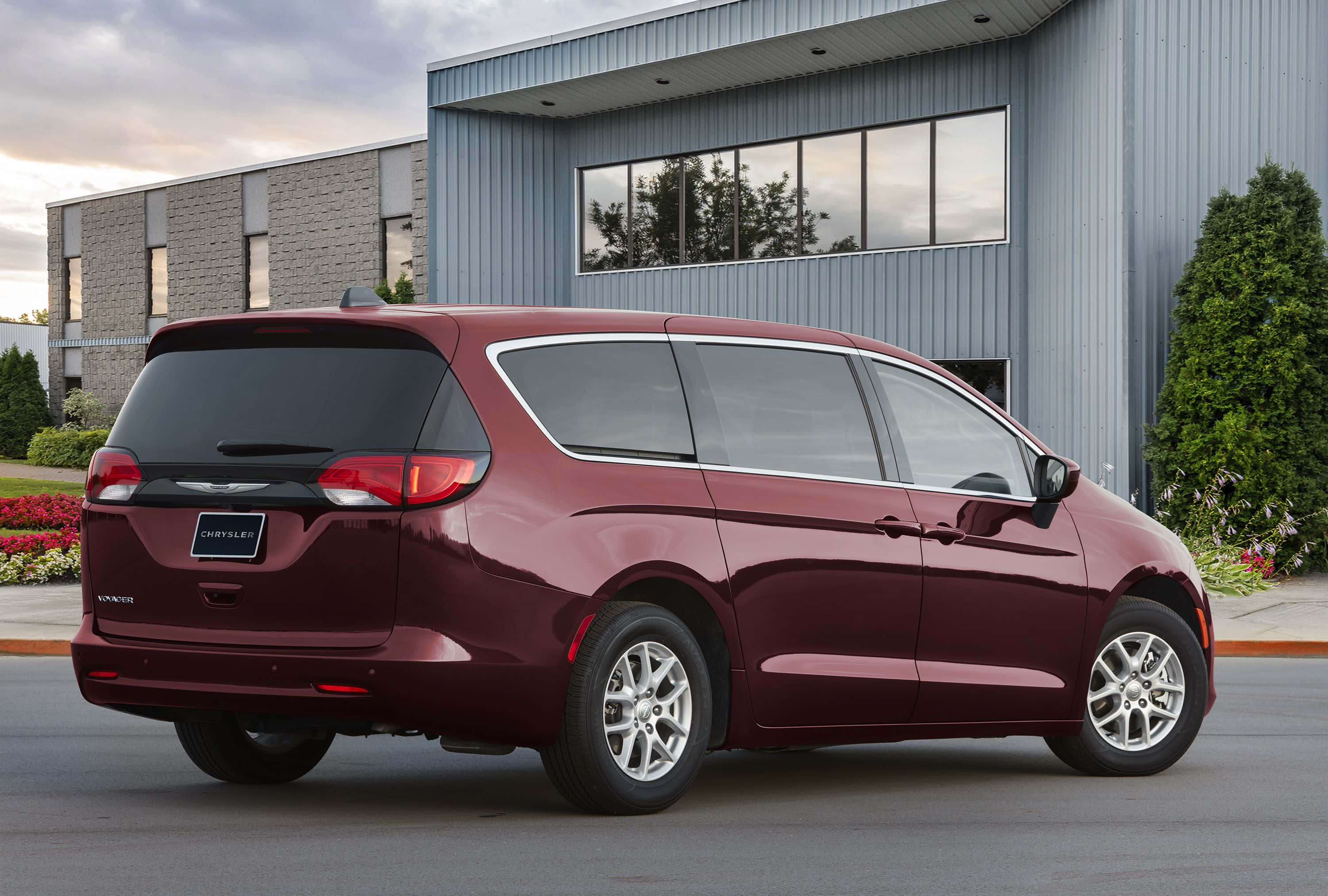 Chrysler Voyager 桌布 壁紙 — 一輛光亮的栗色Chrysler Pacifica小型貨車在黃昏時停泊在現代工業建築外。