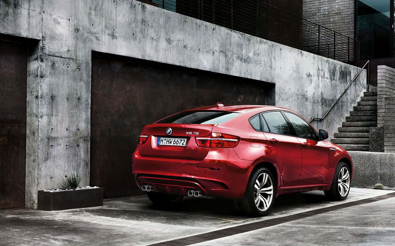 Bmw X6 桌布 壁紙 — 一輛光澤的紅色BMW X6停放在混凝土牆和樓梯旁邊的都市環境中。