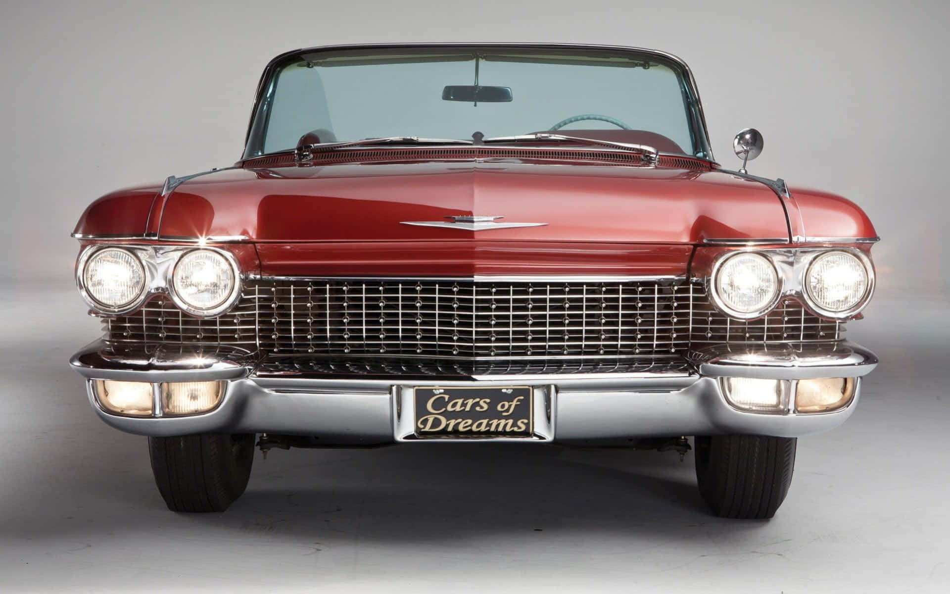 Cadillac Eldorado 桌布 壁紙 — 一輛光澤的紅色經典汽車，帶有鍍鉻格柵和四個圓形頭燈，正面朝向純灰色工作室背景。