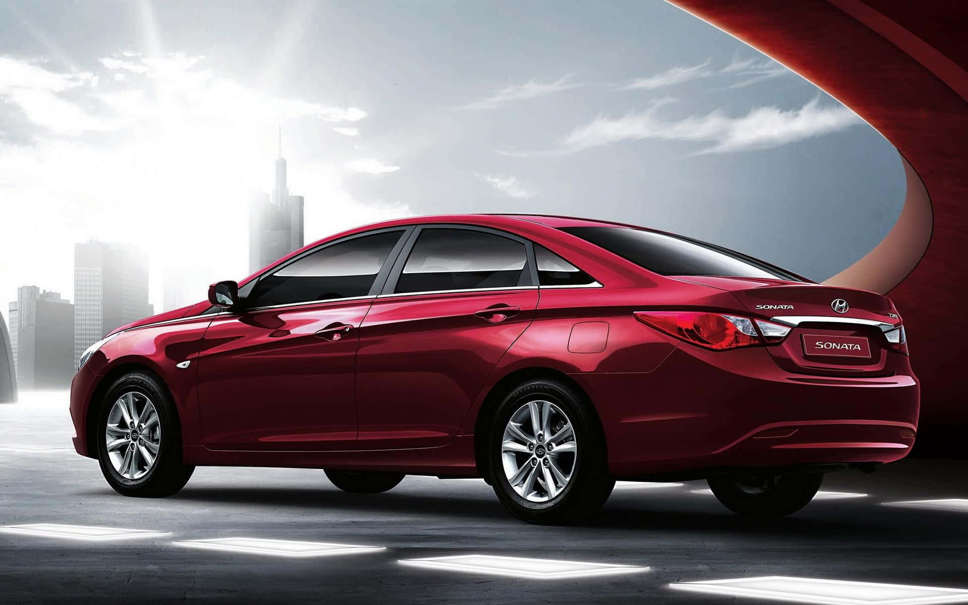 Hyundai Sonata 桌布 壁紙 — 一輛光澤的紅色現代索納塔轎車在明亮的陽光下閃耀，背景是現代城市天際線和彎曲的建築結構。