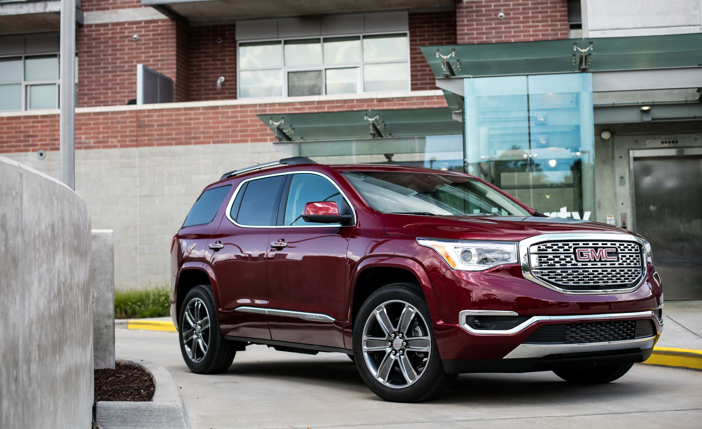 Gmc Acadia 桌布 壁紙 — 一輛光澤的棗紅色GMC Acadia SUV停放在現代磚和玻璃建築入口處。