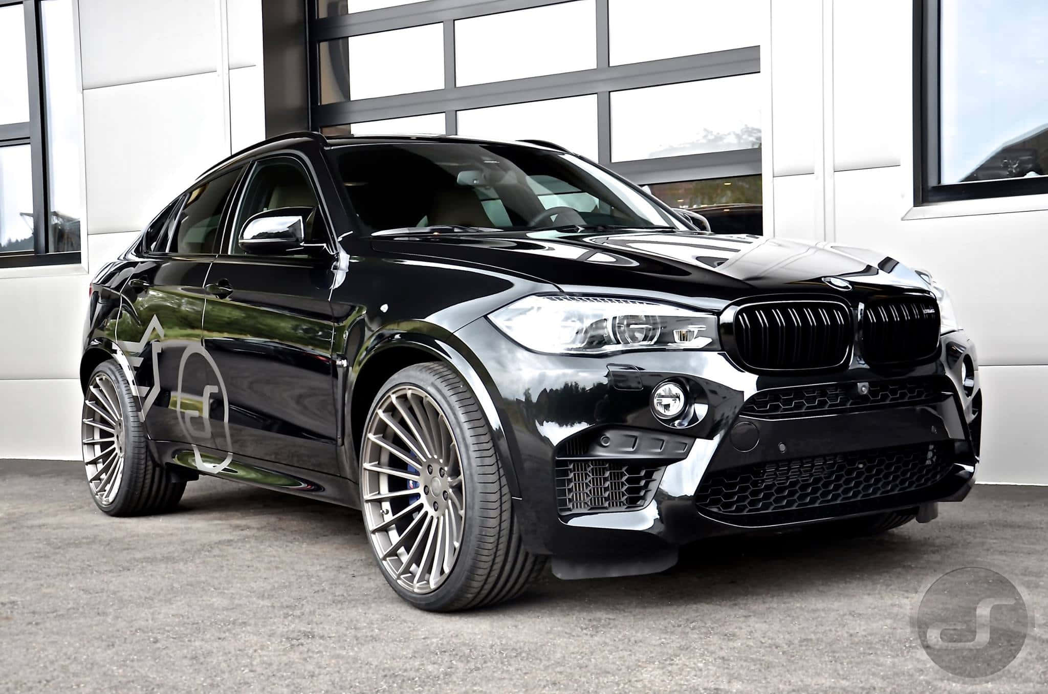Bmw X6 桌布 壁紙 — 一輛光澤黑色BMW X6 M配備訂製銀色輪圈，停放在現代白色車庫內。